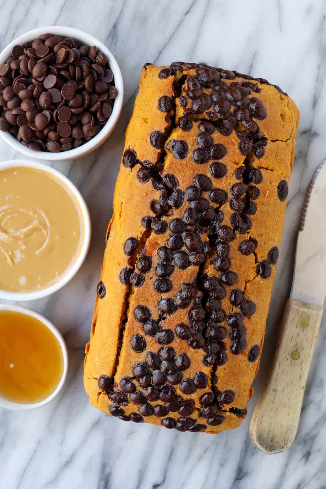 Whole loaf of sweet potato bread. Chocolate chips, peanut butter and honey in small dishes on the side for decoration.