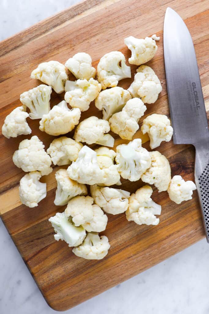Raw chopped cauliflower florets on cutting board with knife.