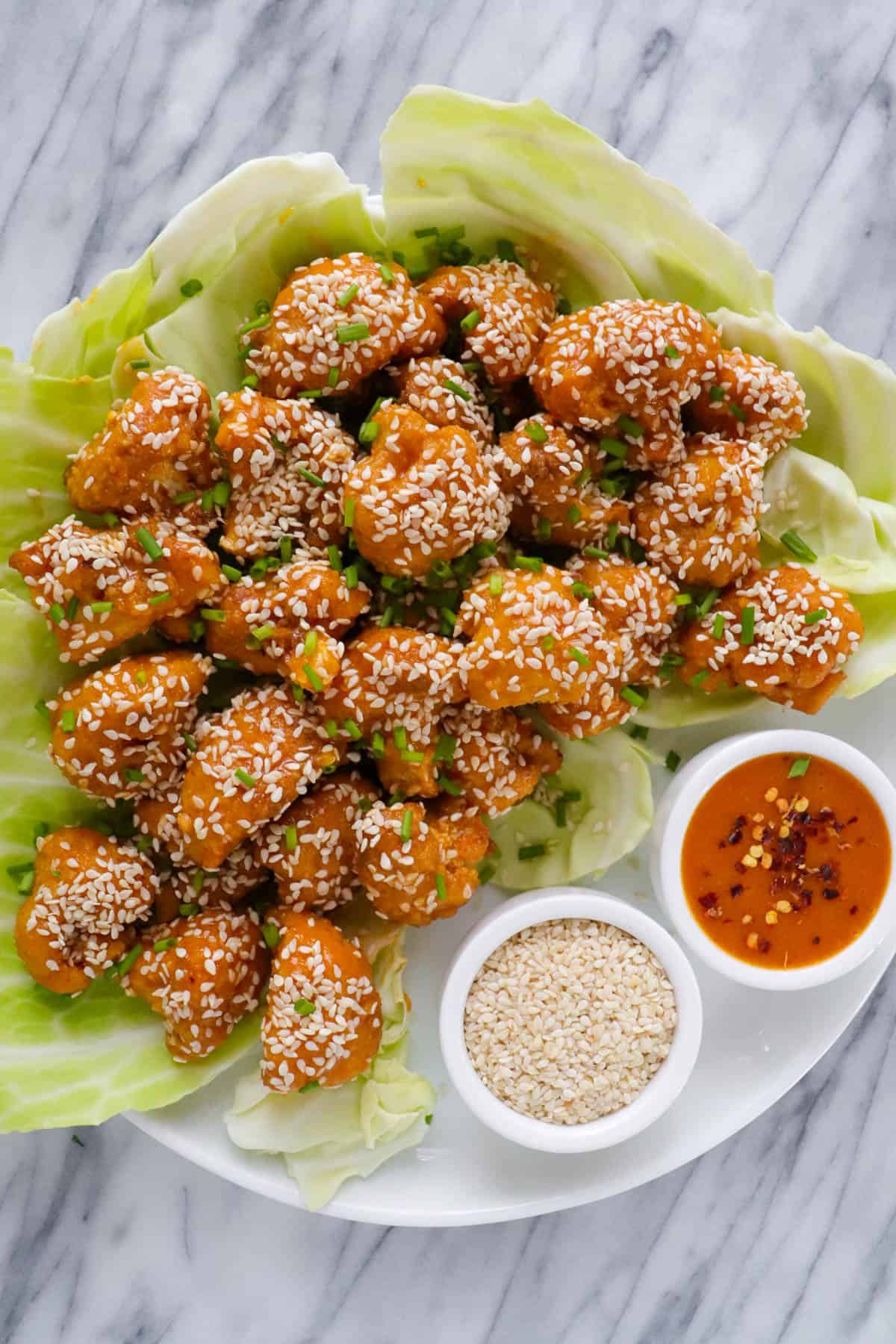 Baked cauliflower wings on plate with sesame seeds and extra sauce.