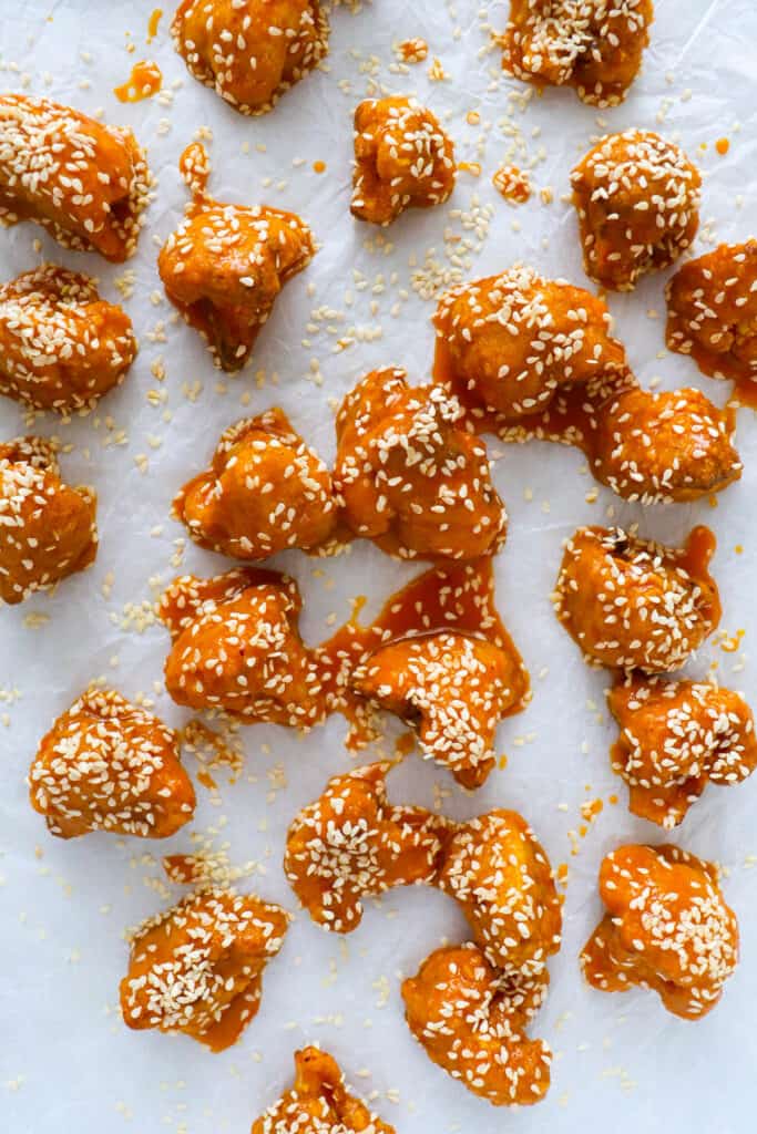 Cauliflower wings sprinkled with sesame seeds on baking paper.