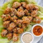 Baked cauliflower wings on plate with sesame seeds and extra sauce.
