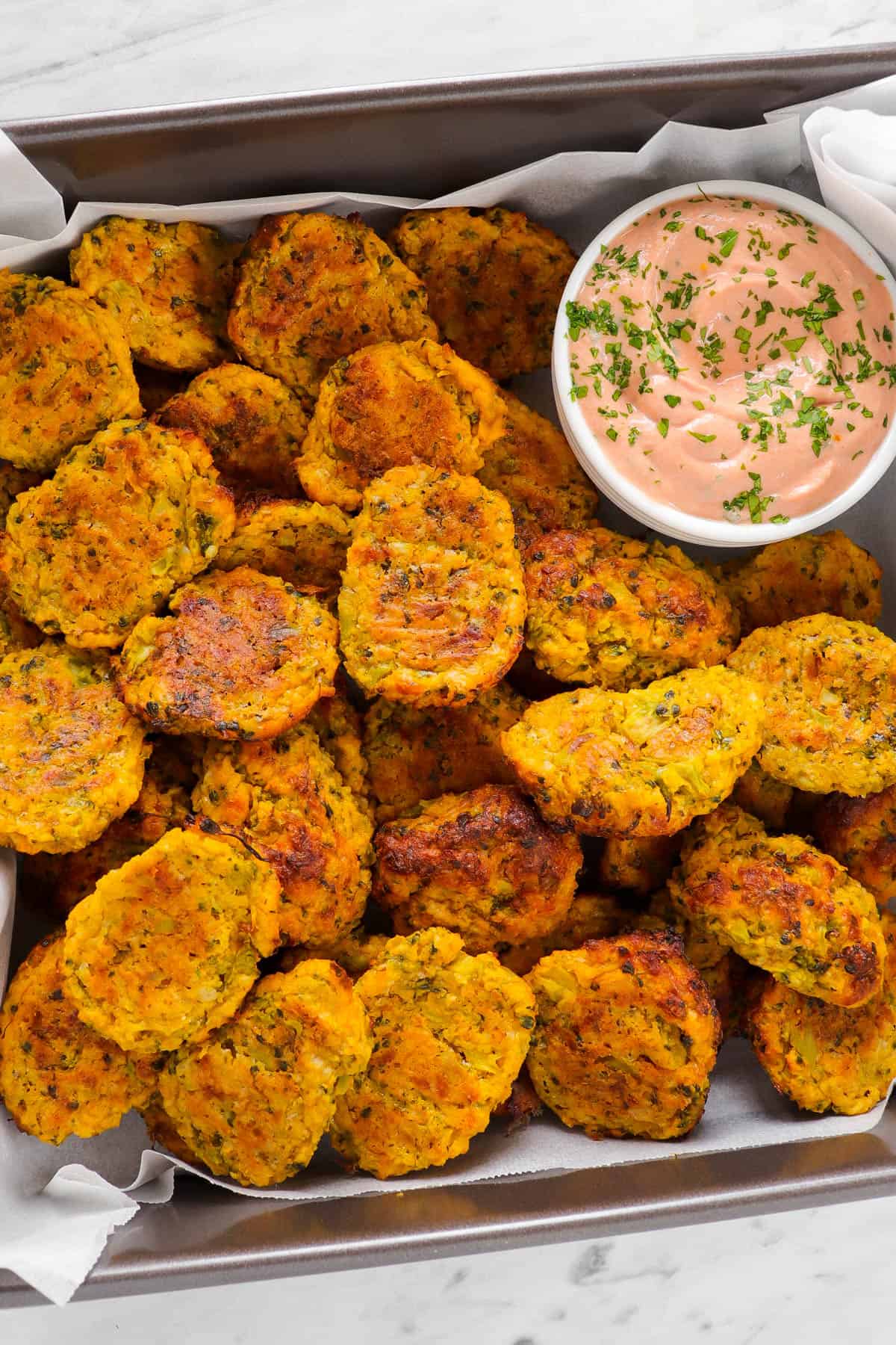 Baked broccoli tots in baking tin with sauce for decoration.