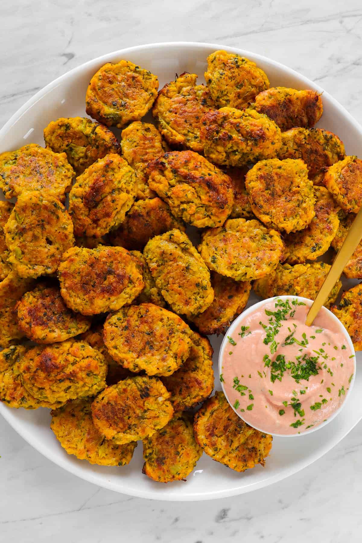 Baked broccoli pumpkin tots on a plate with tomato yoghurt sauce and golden spoon.