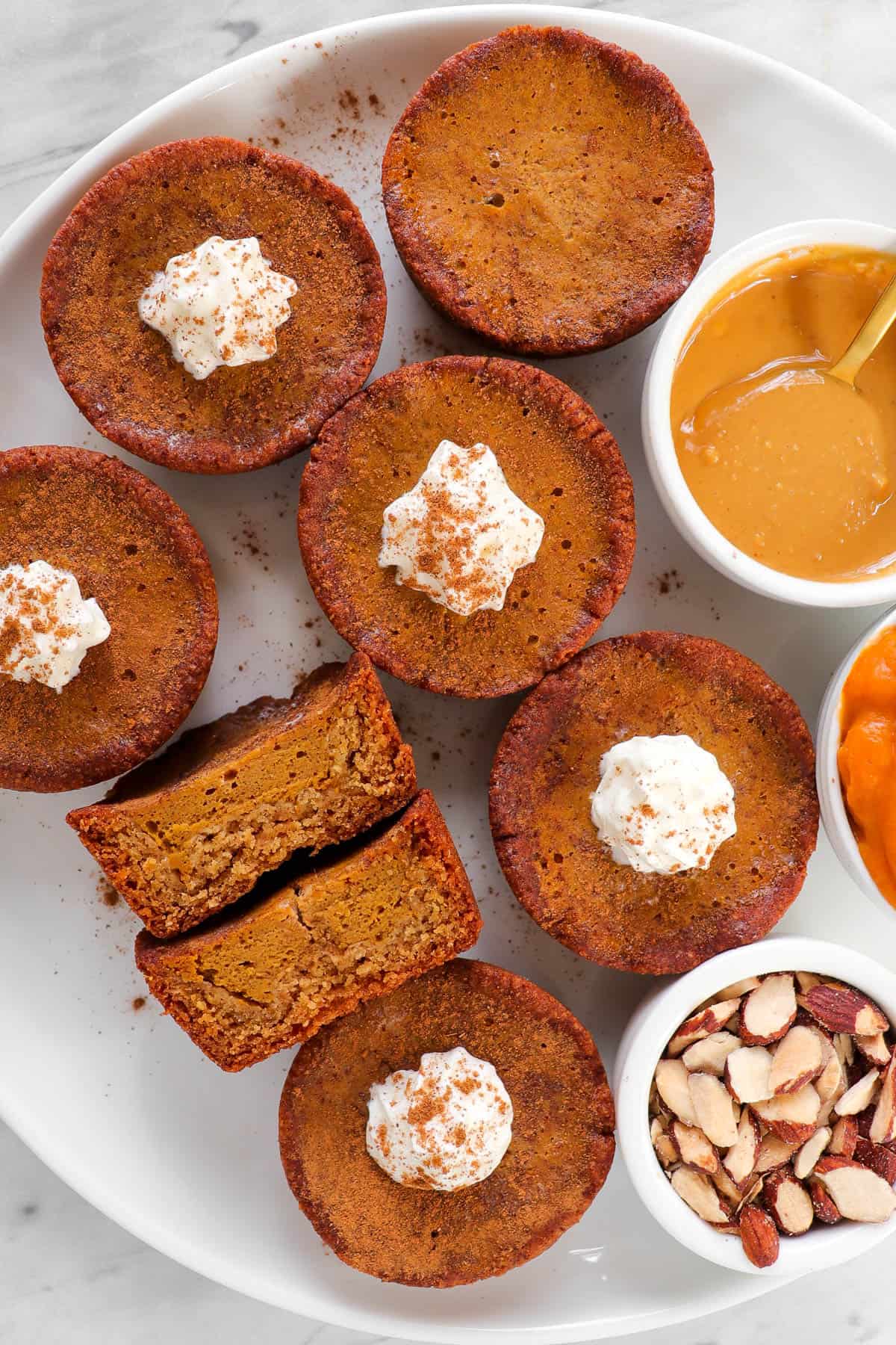 Cooked pies on a plate with mini bowls of peanut butter, almonds and pumpkin puree on the side for garnish. One cut slice in half for inside shot.