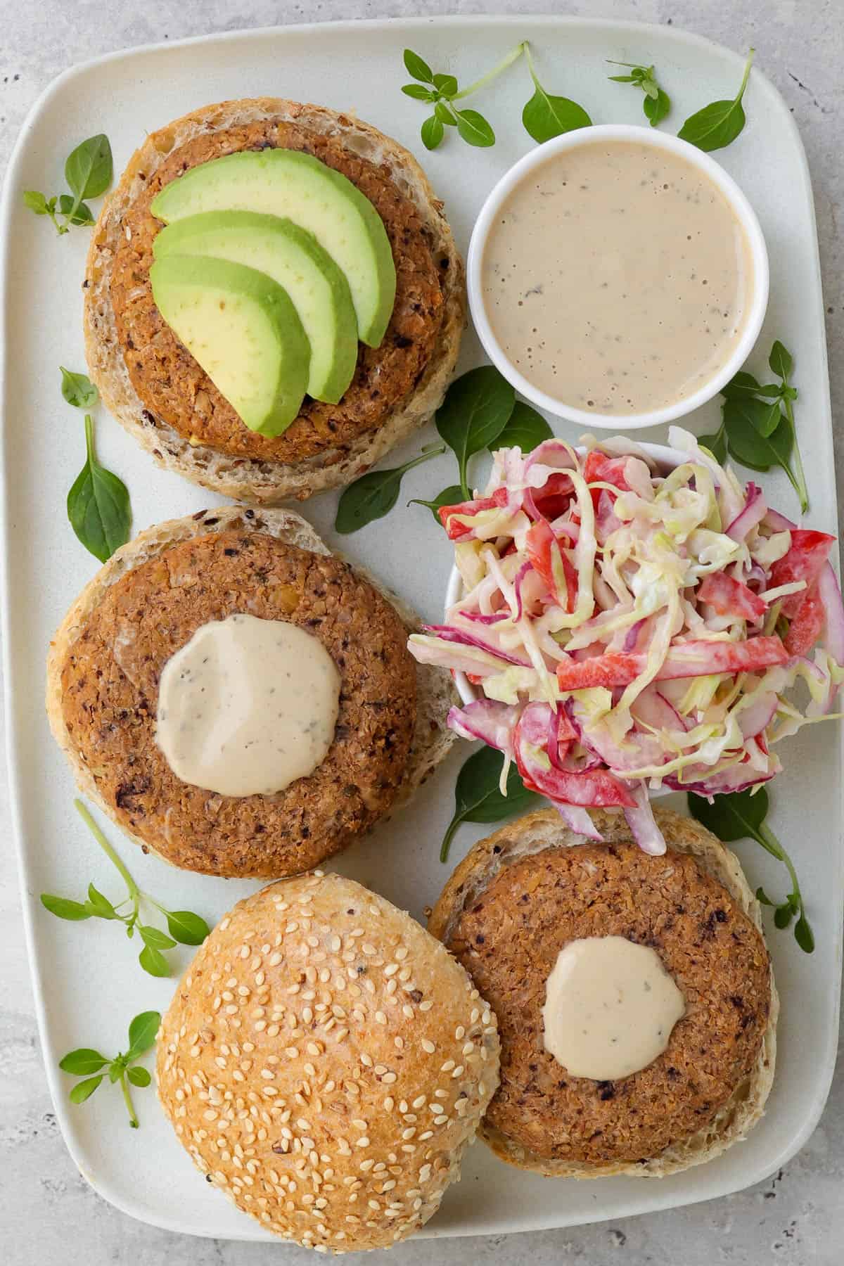 Patties on buns topped with avocado. Slaw and tahini sauce on the side.