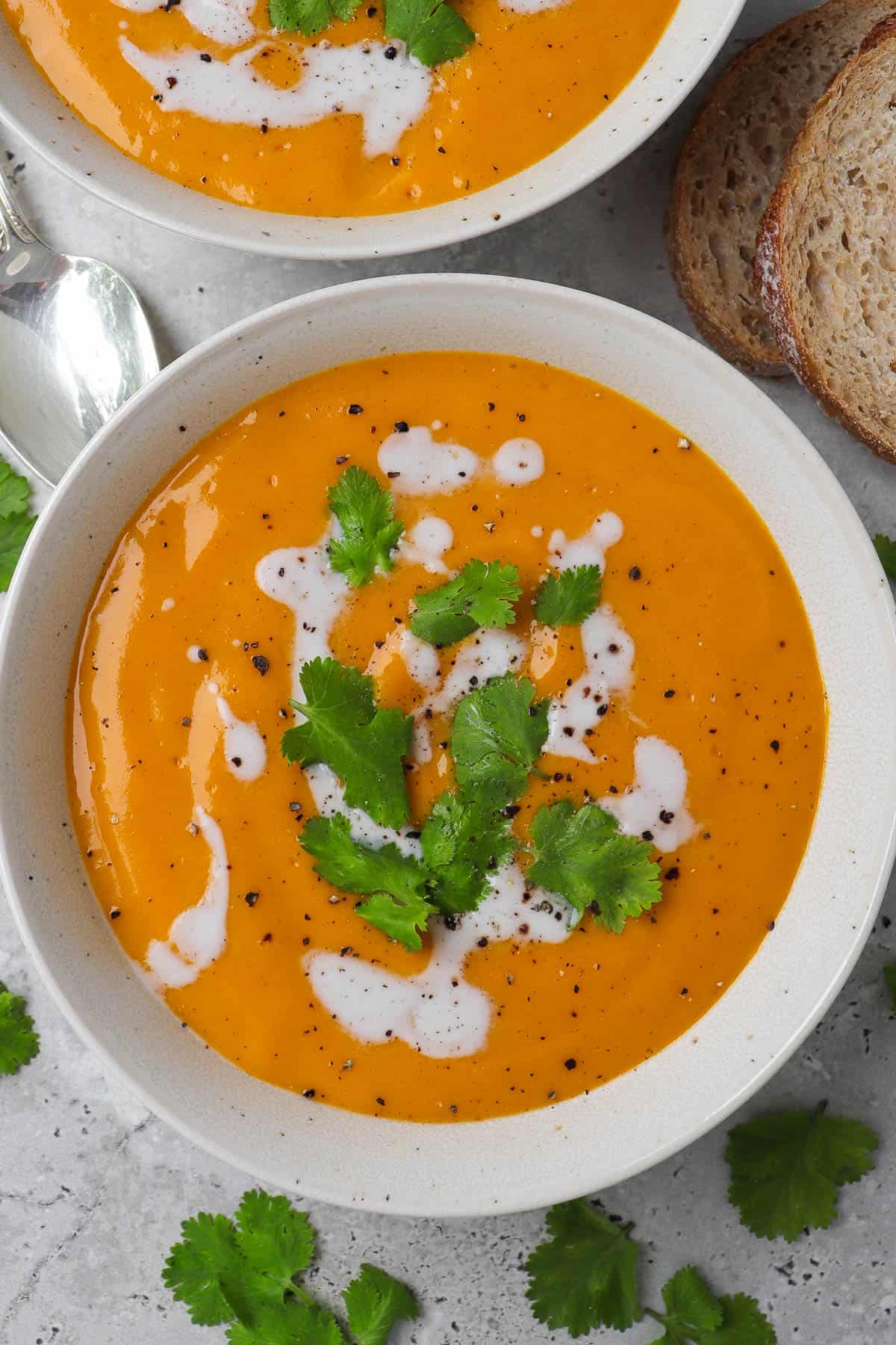 Close up short of soup in a bowl with coconut milk drizzled and coriander leaves on top. Spoon on side.