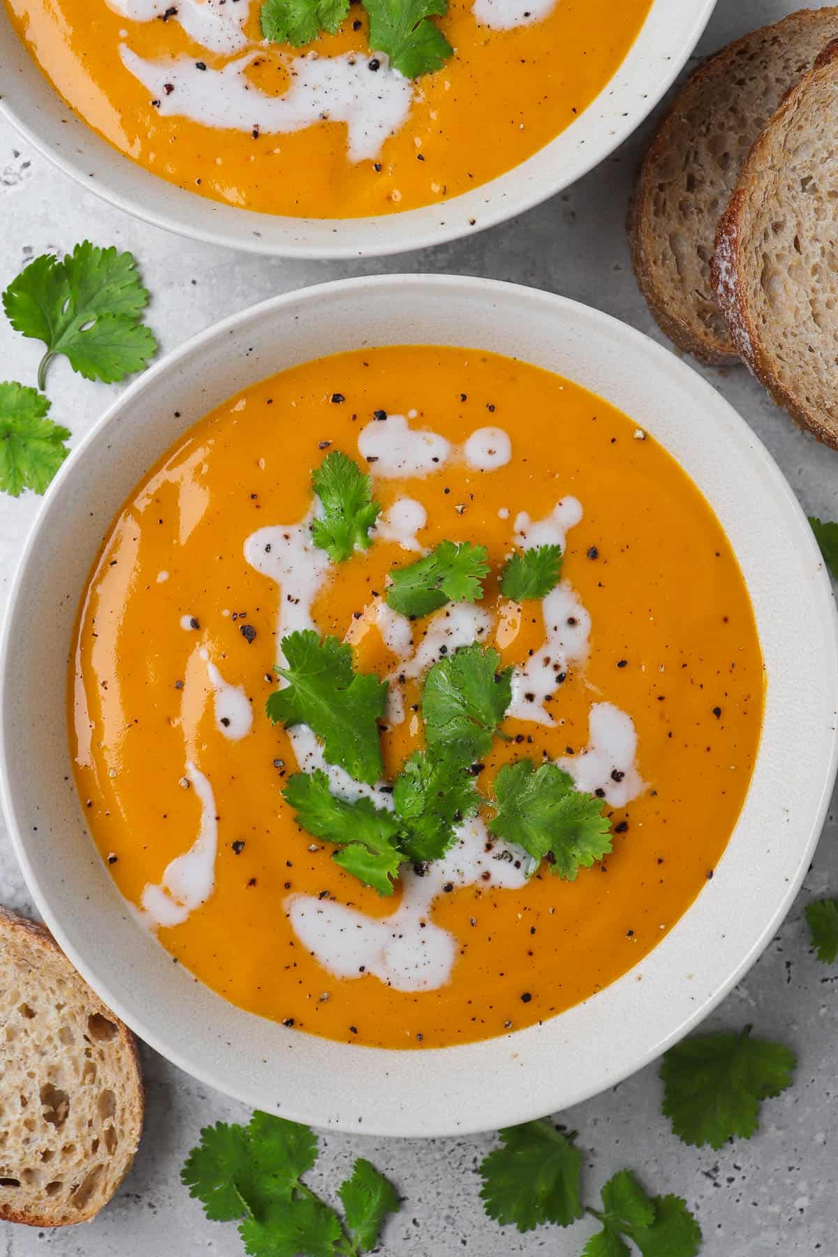 Close up short of carrot swede soup in a bowl with coconut milk drizzled and coriander leaves on top.