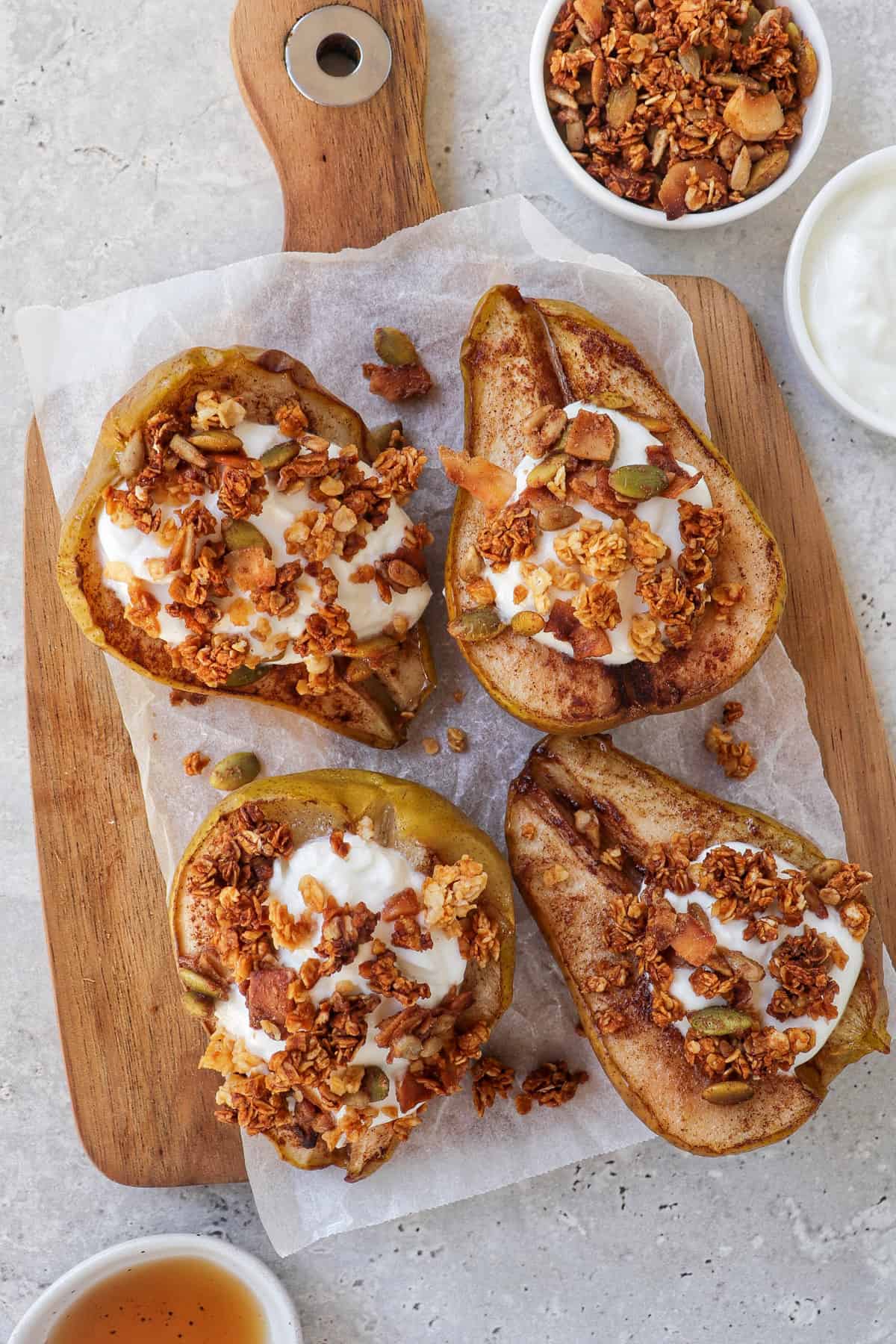 close up shot of baked pears on wooden board topped with plain yoghurt and granola.