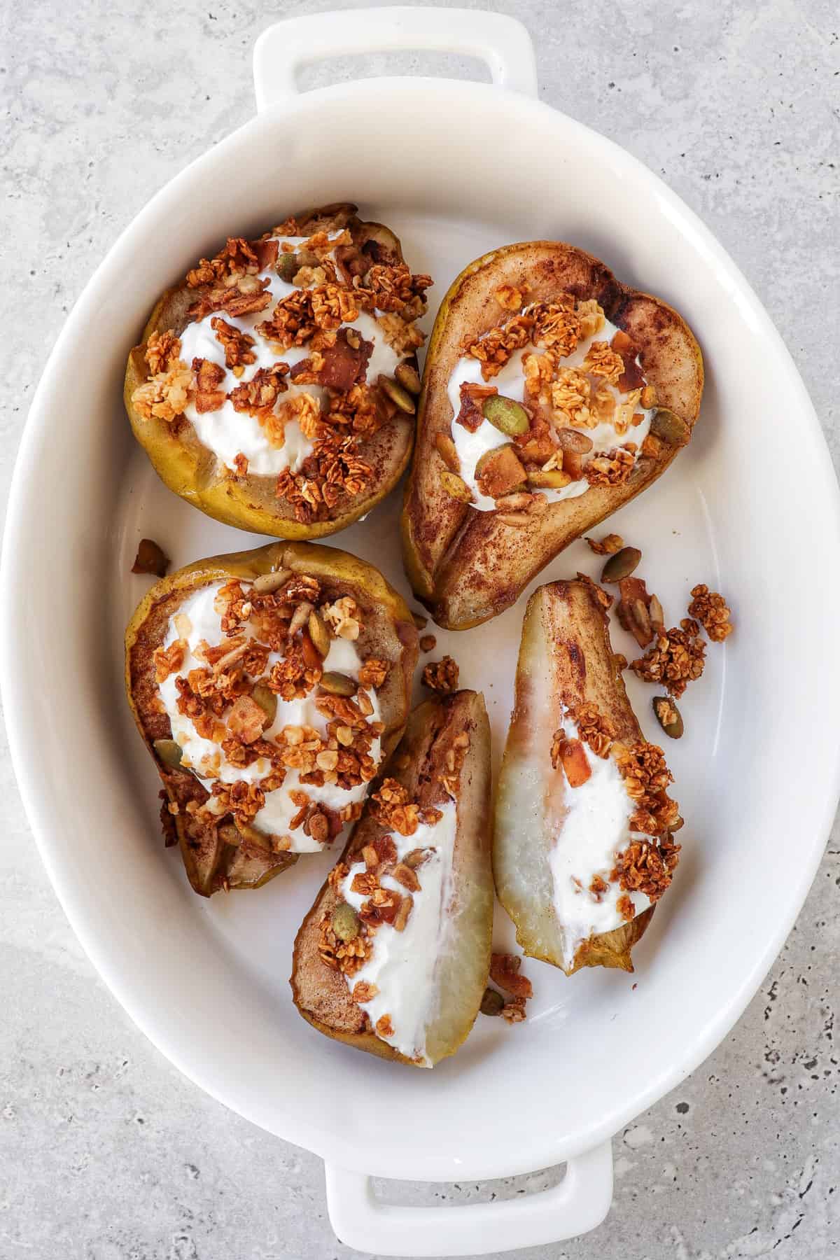 Cooked pears in a white oval dish topped with greek yoghurt and sprinkle of granola.