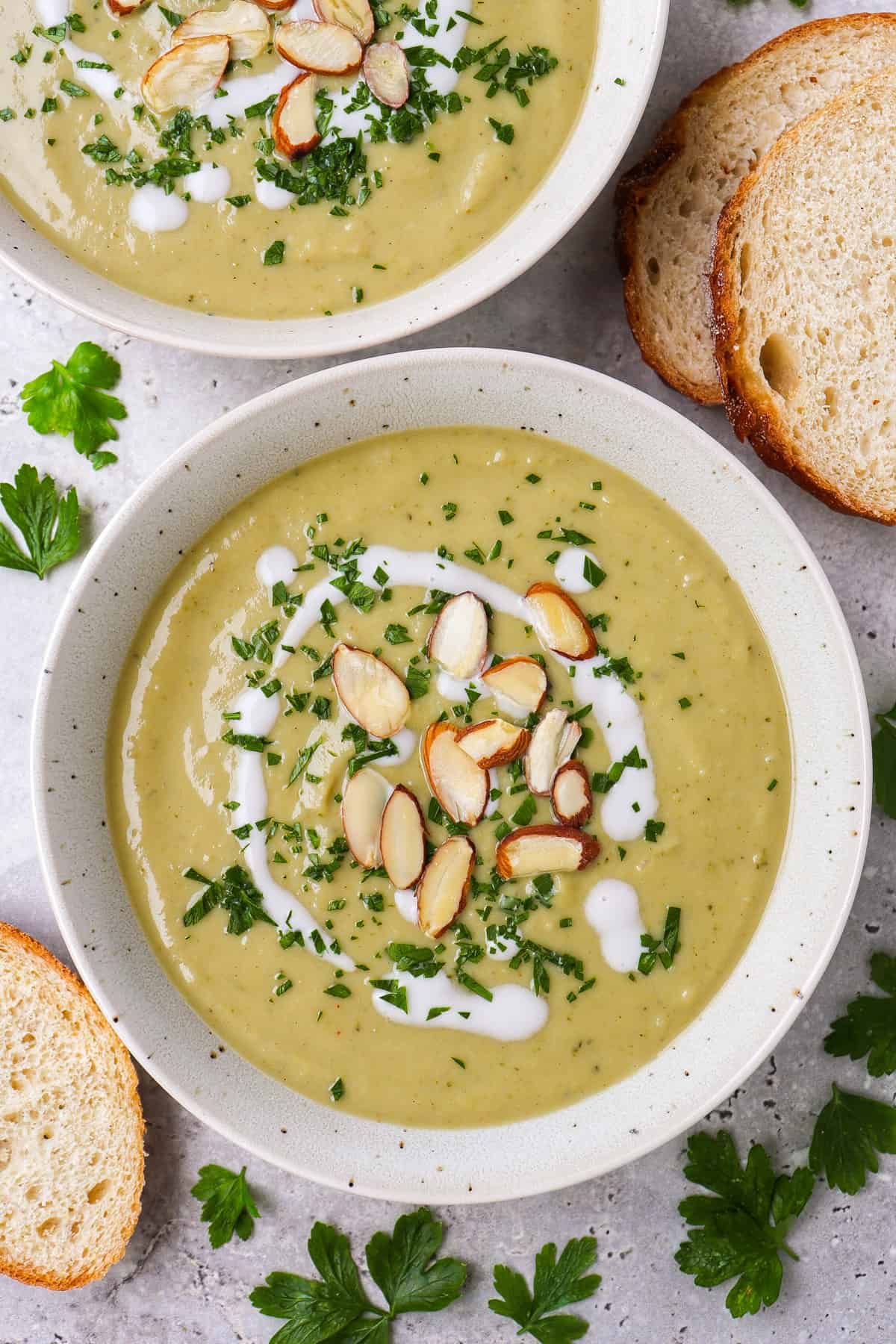 Broccoli soup in 2 bowls topped with coconut cream. almond flakes, finely chopped parsley.
