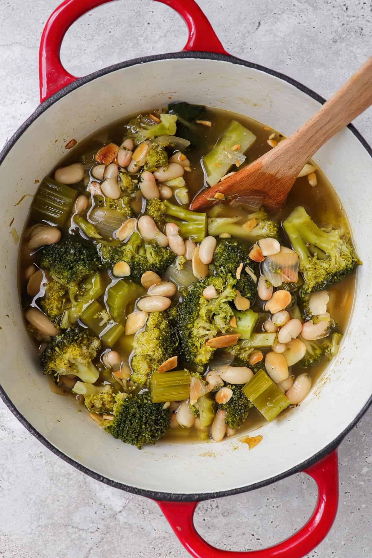 Large of pot of cooked broccoli, celery, white beans, flake almonds and wooden spoon before being blended.