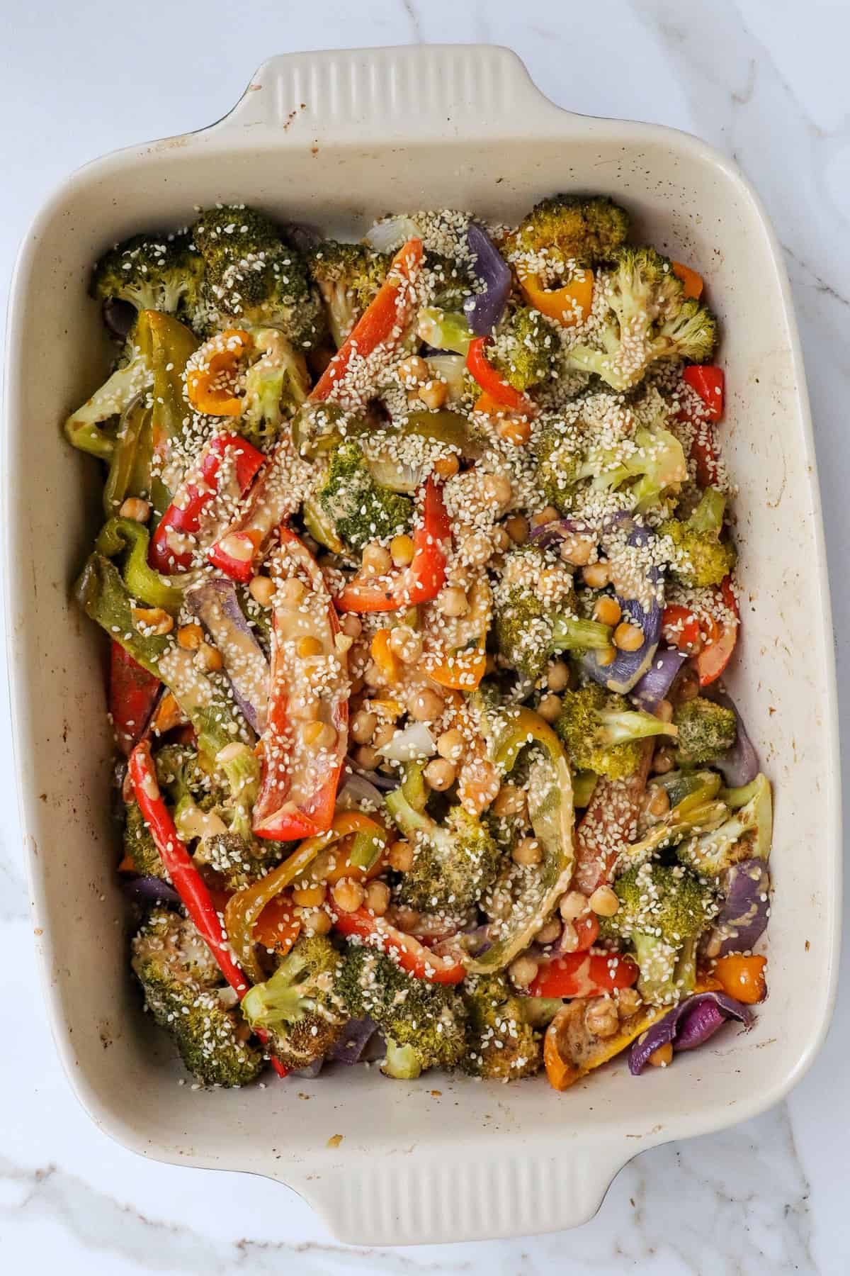Baked chickpeas and veggies in dish with sesame seeds.