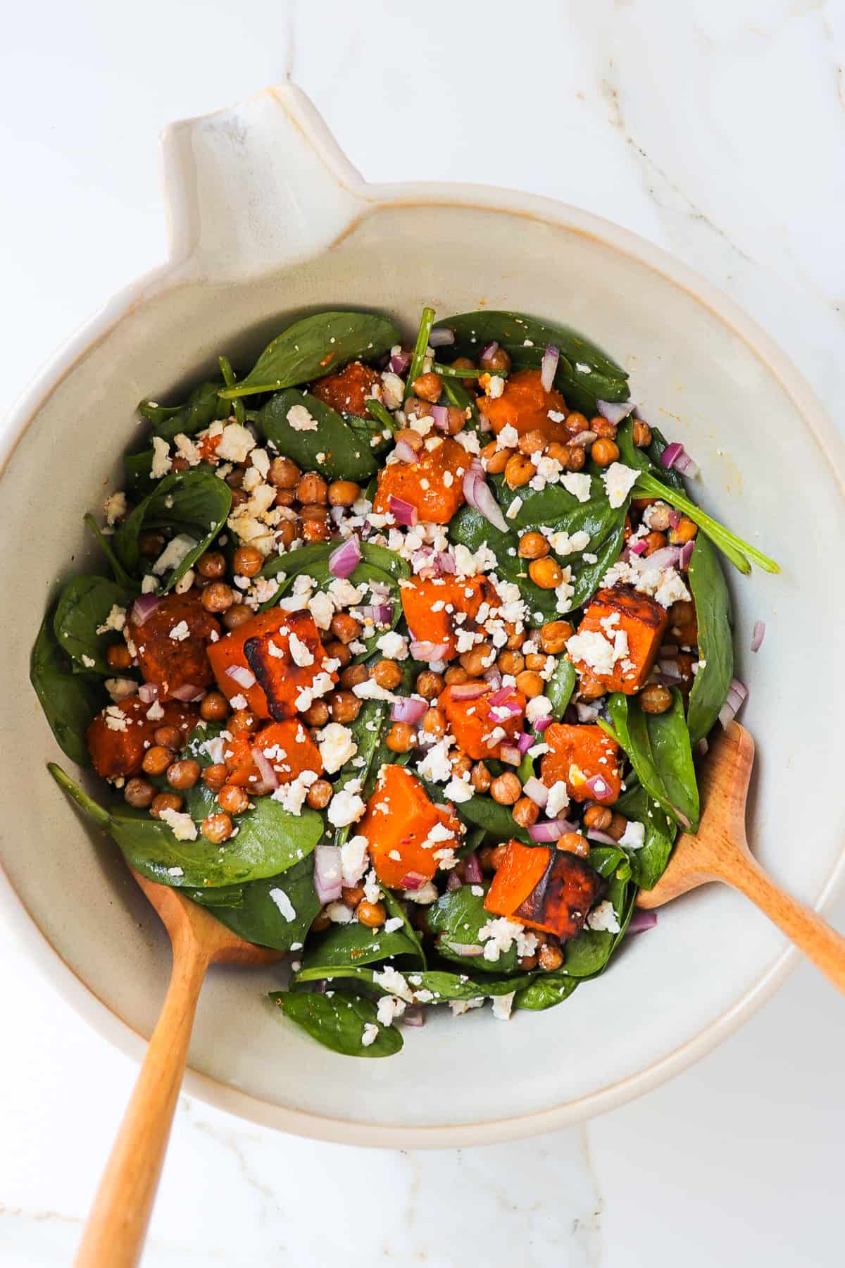 Salad in a mixing bowl with wooden spoons.