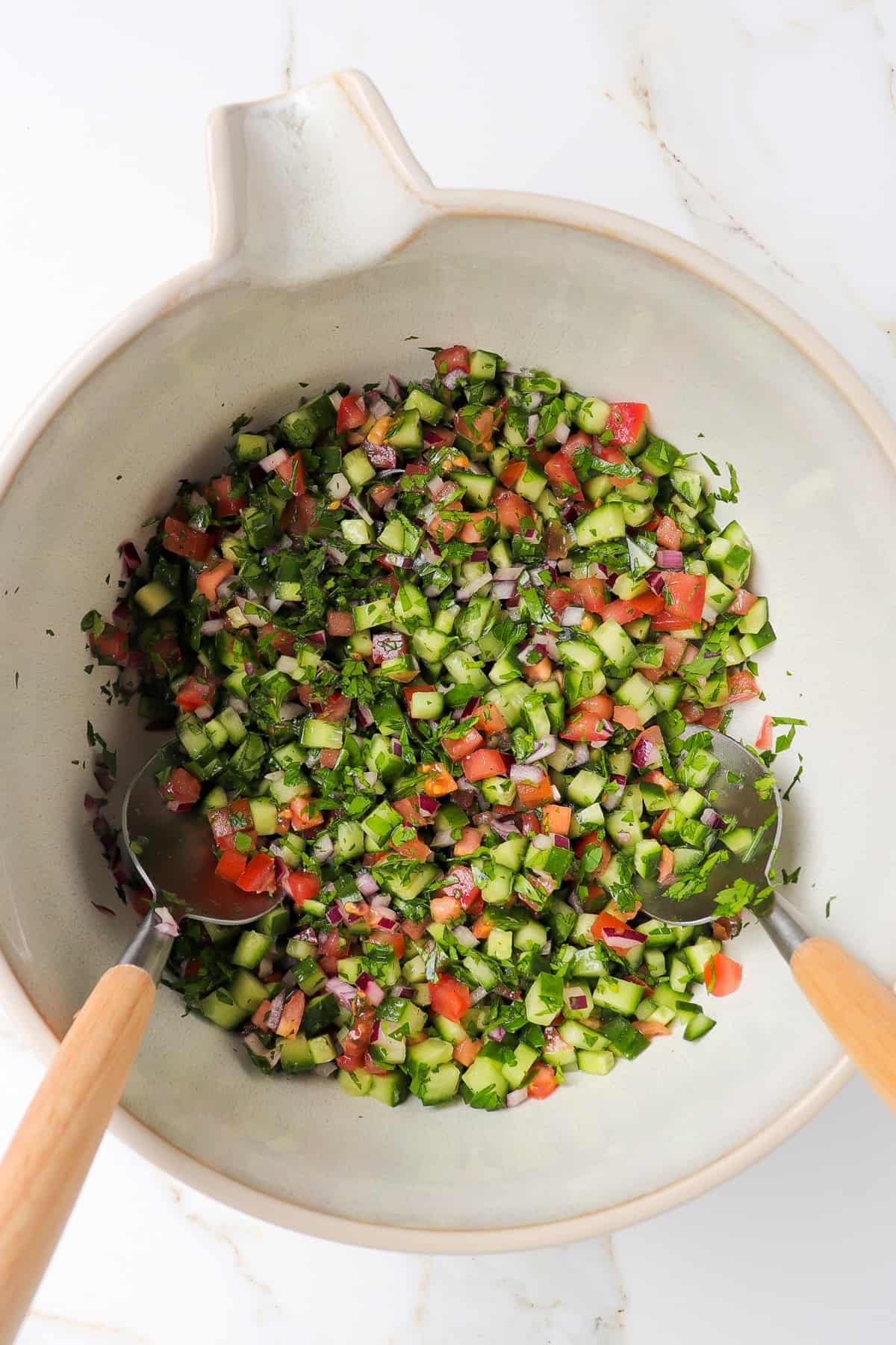 Jerusalem salad in a mixing bowl with wooden spoons.