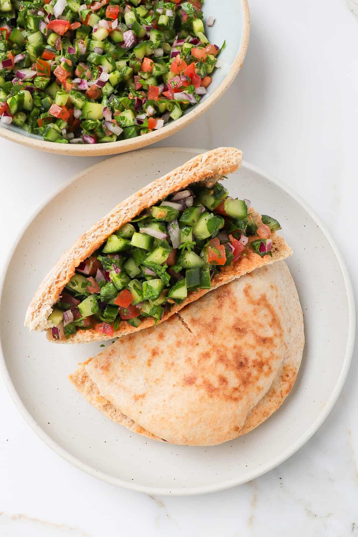 Jerusalem salad stuffed into pita pockets on a plate.