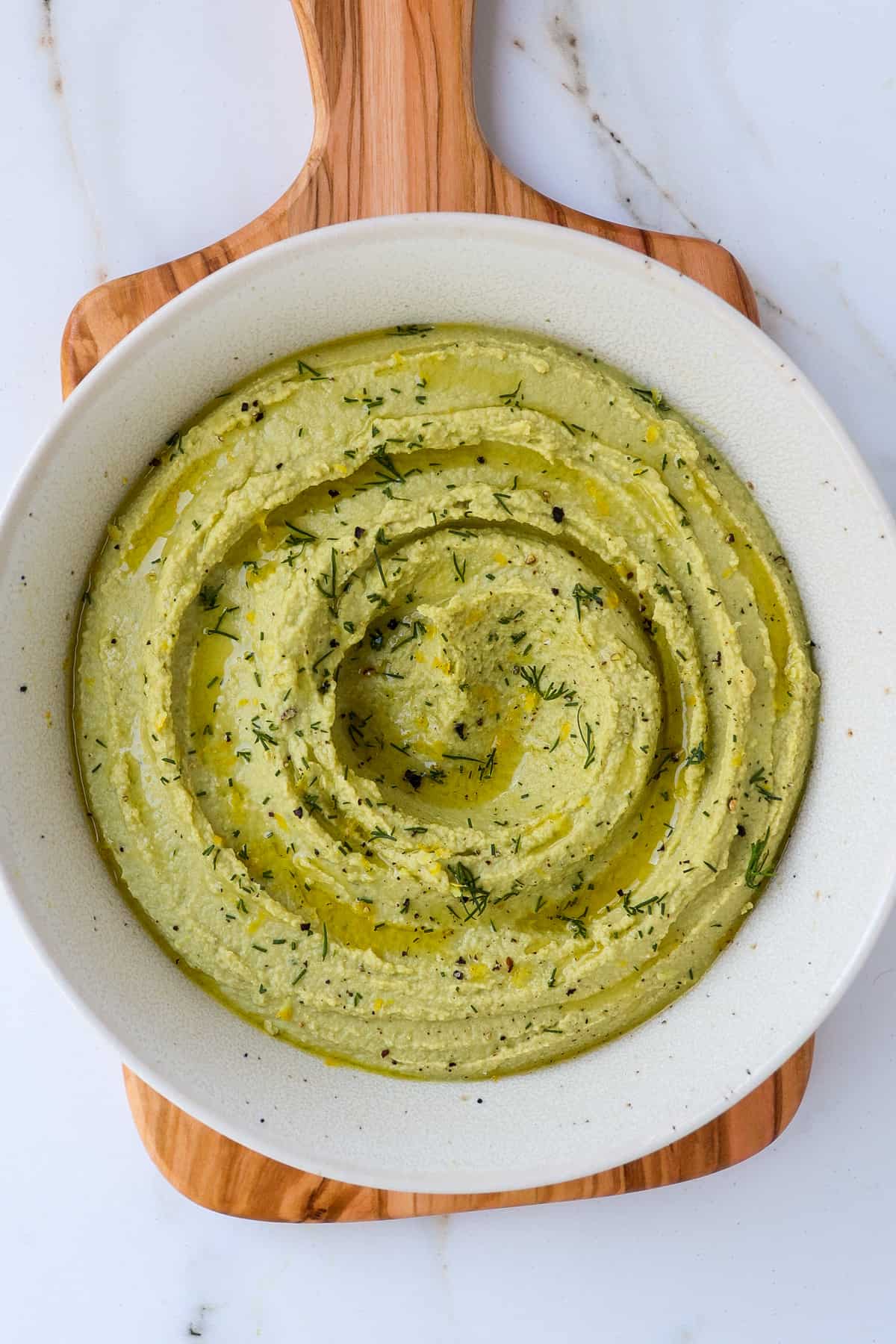 Lemon dill hummus in a bowl on wooden board.
