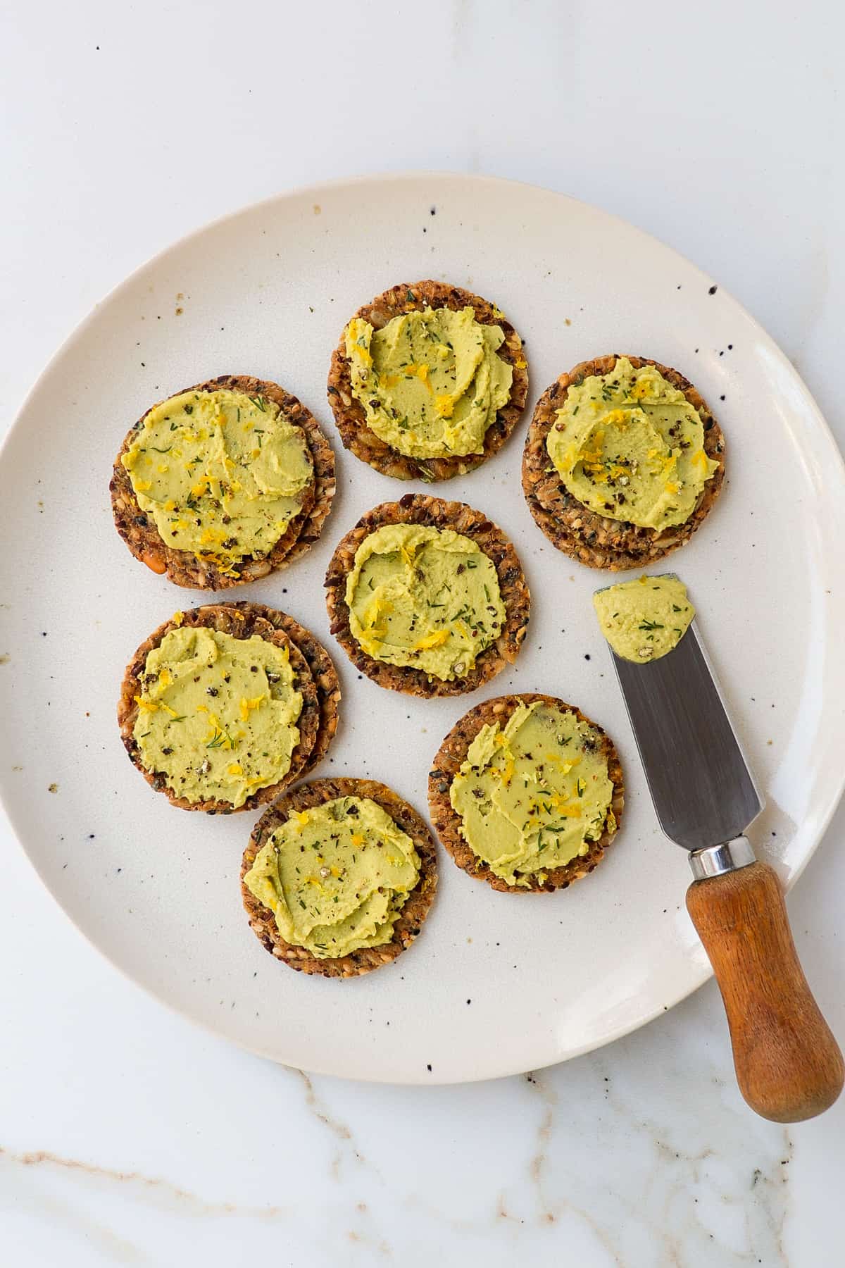 Crackers on a plate spread with dill hummus.