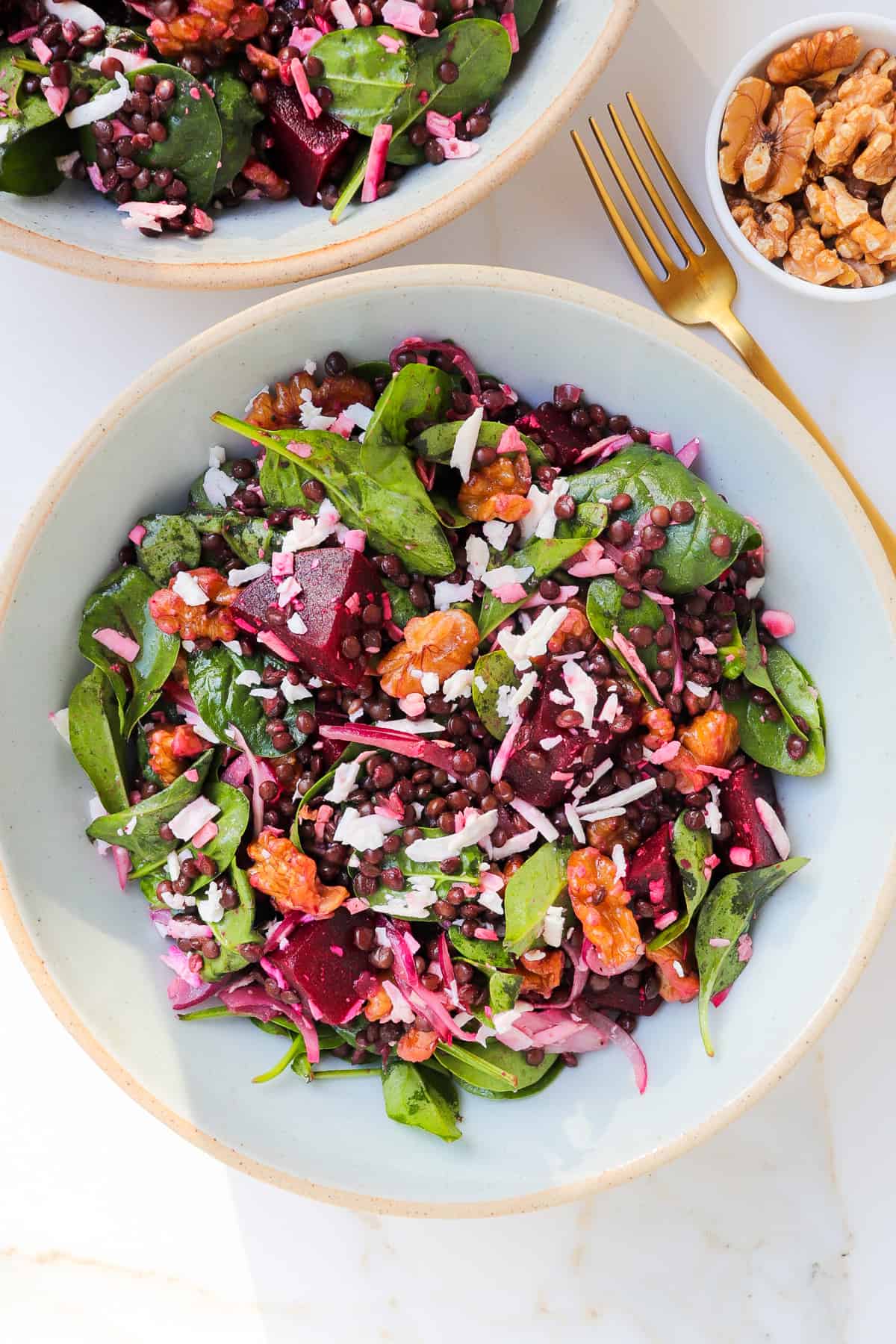 Beetroot salad served in a bowl with a gold fork and walnuts on the side.
