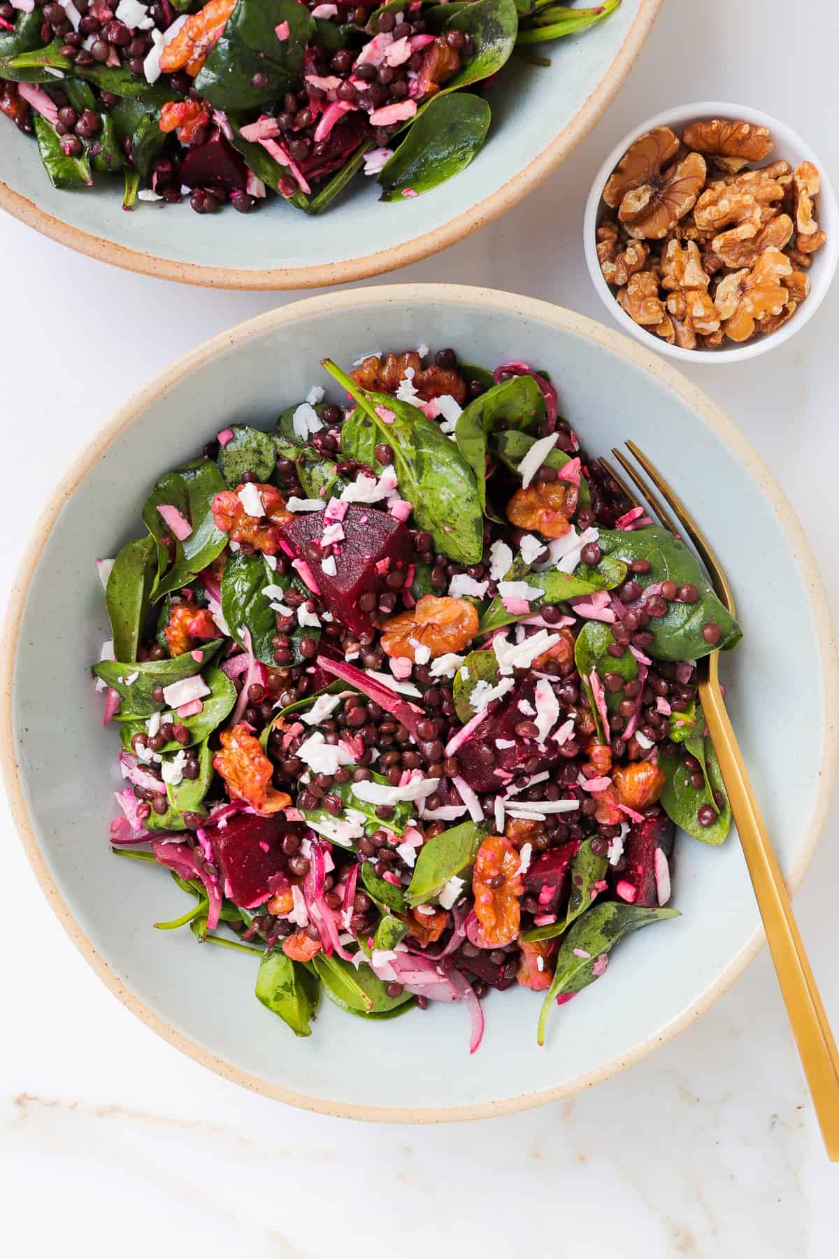 The salad served in a bowl with a gold fork and walnuts on the side.