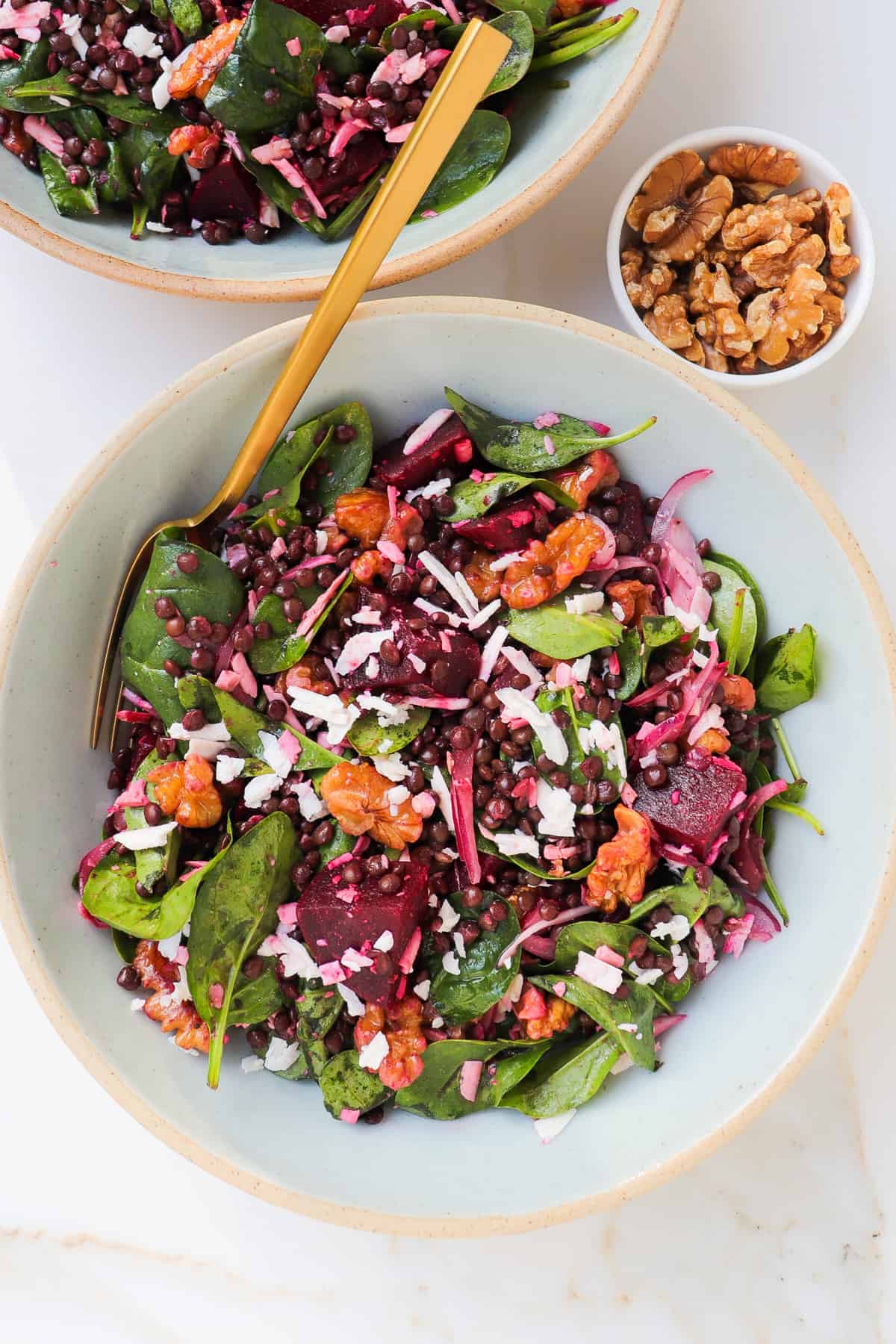 Beetroot salad served in a bowl with a gold fork and walnuts on the side.