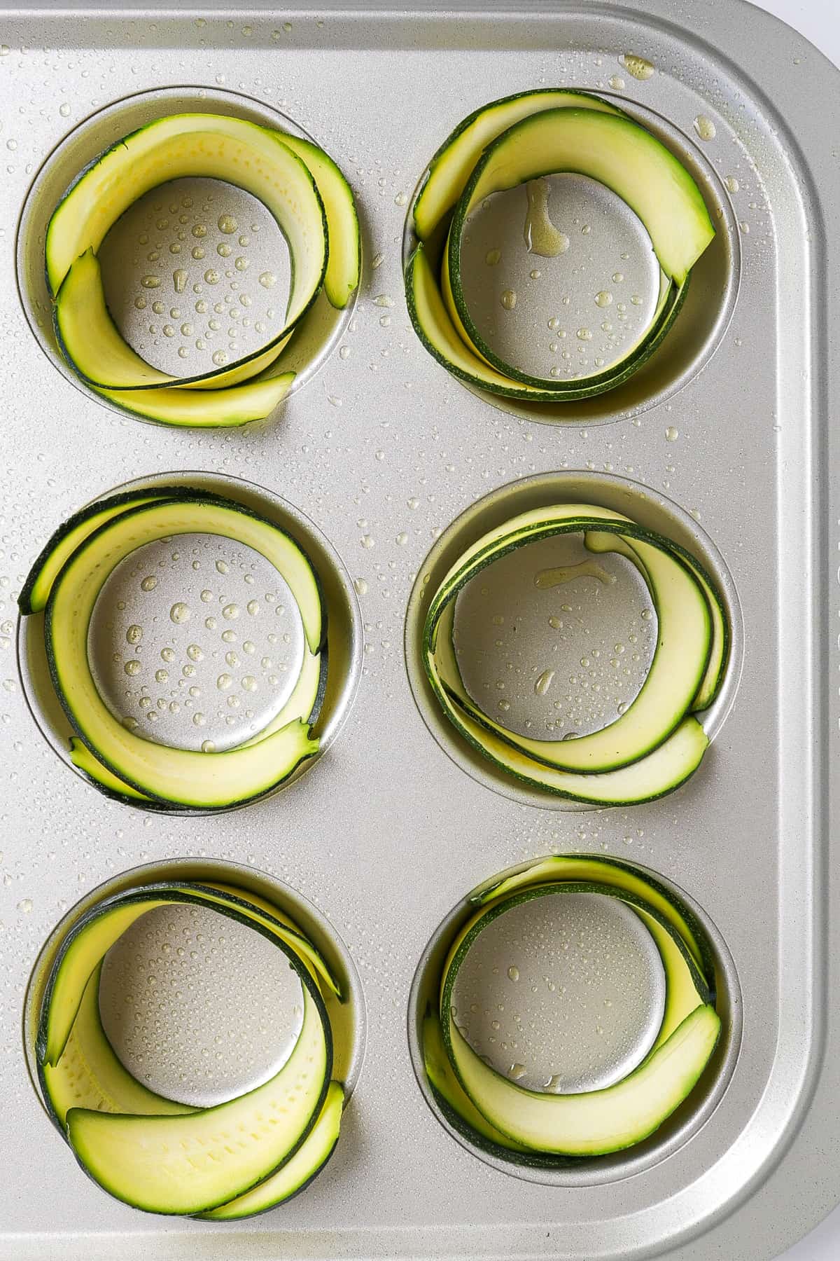 Muffin pan with zucchini strips wrapped around each cavity.