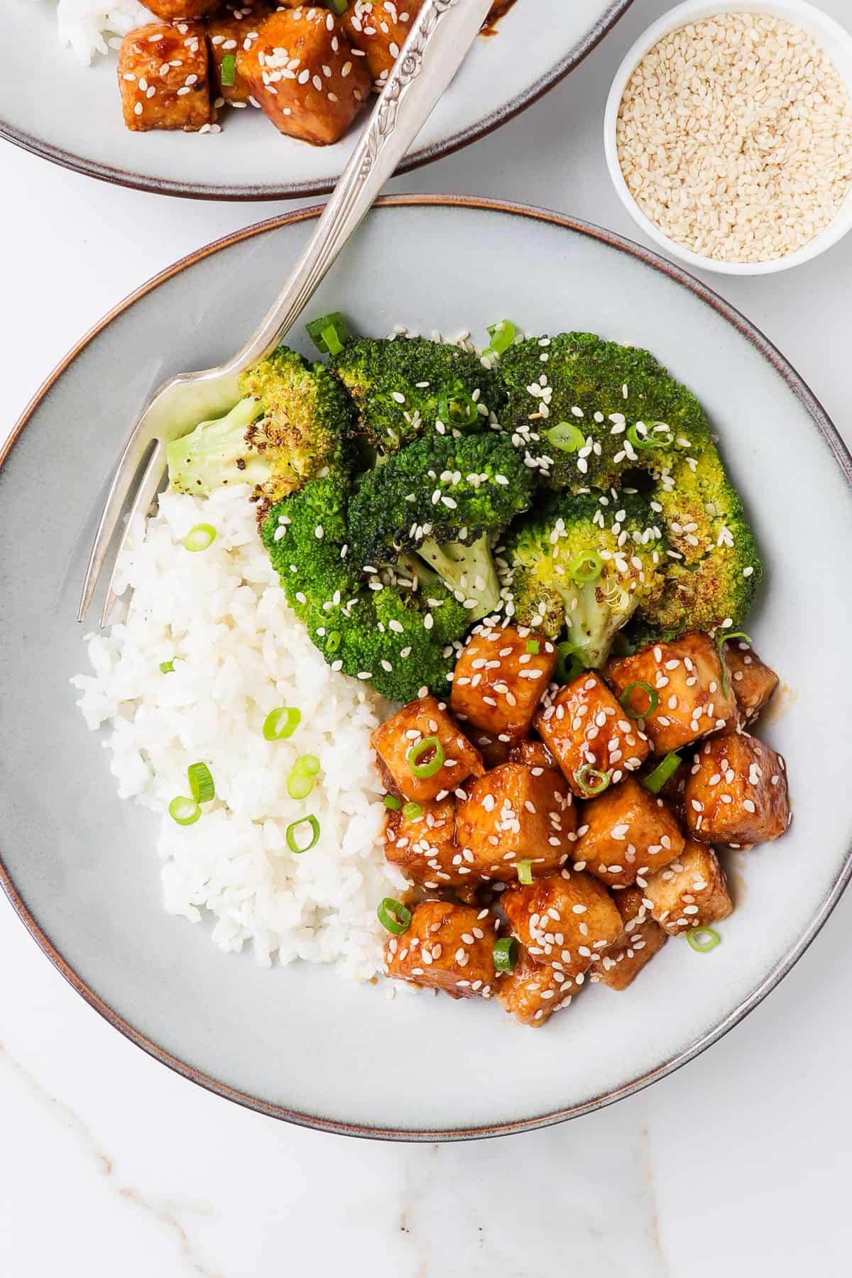 Honey garlic tofu in a bowl with a fork, roasted broccoli and rice.