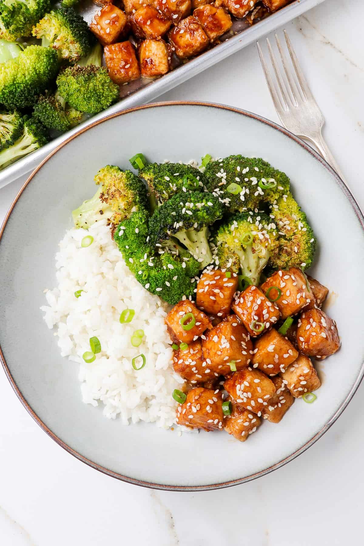 Honey garlic tofu in a bowl with roasted broccoli and rice. Sheet pan on the side.