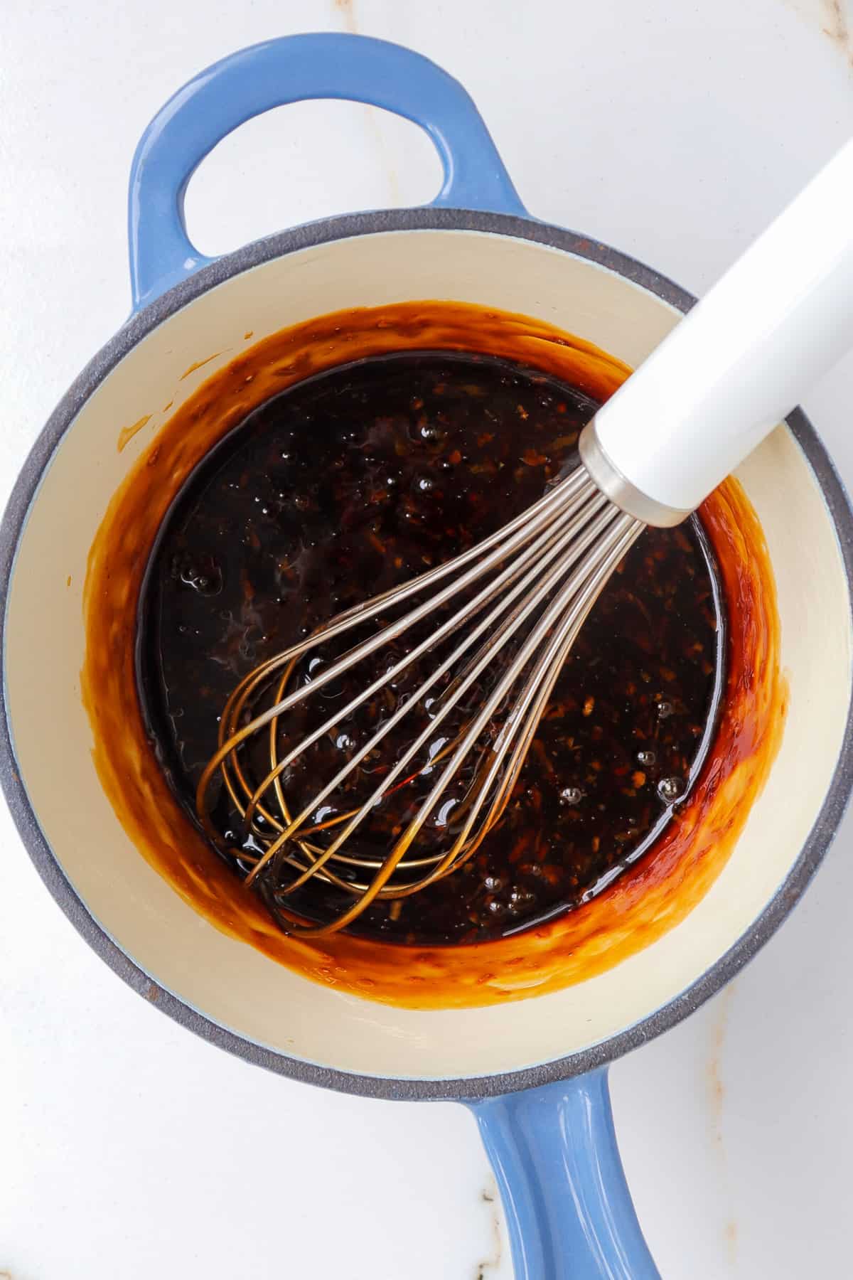 Honey garlic sauce in pot with whisk.