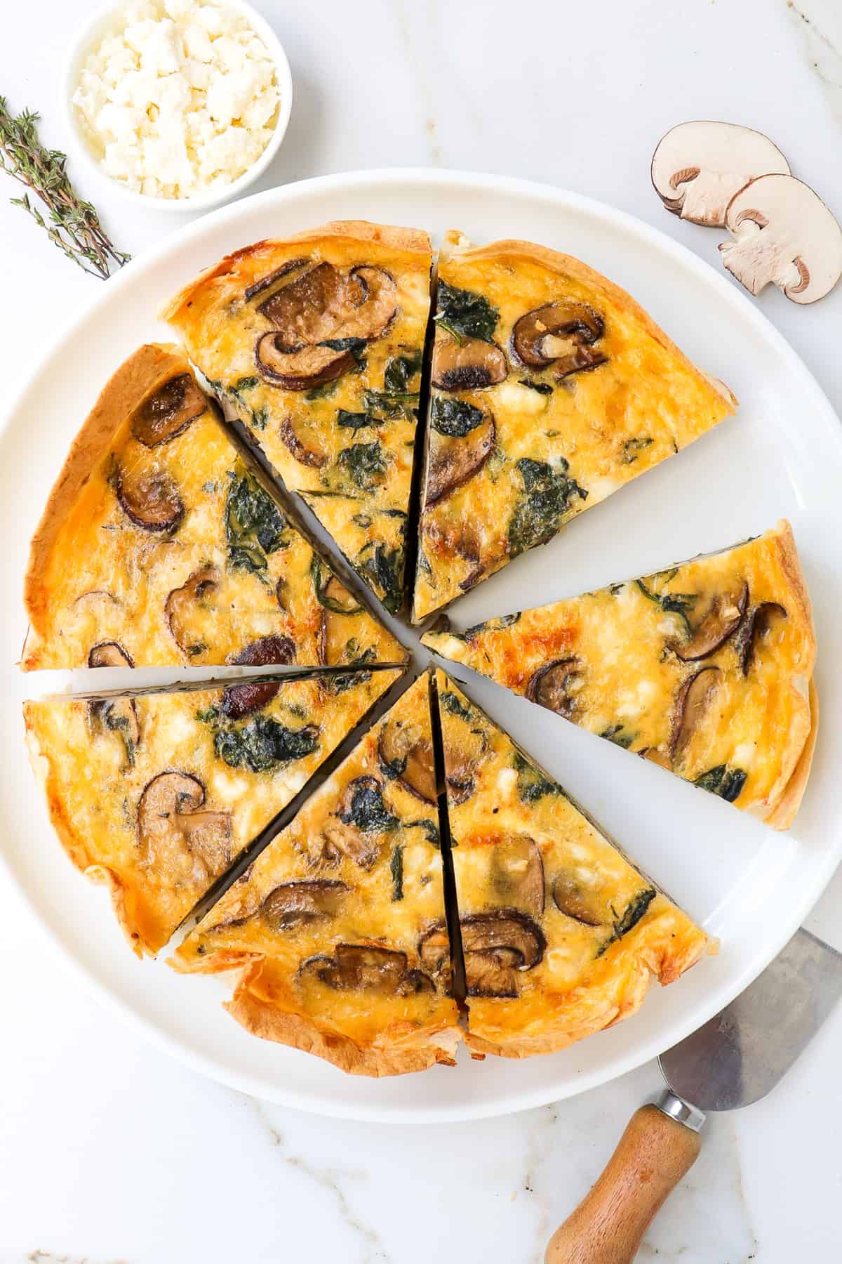 Spinach mushroom quiche sliced up on a plate with pieces separated.