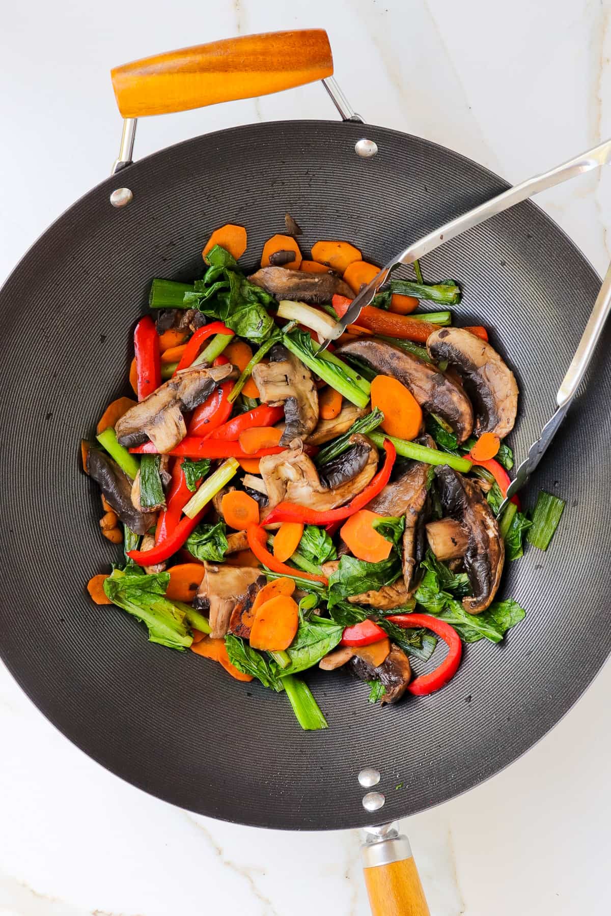 Veggies stir fried in a wok with tongs.