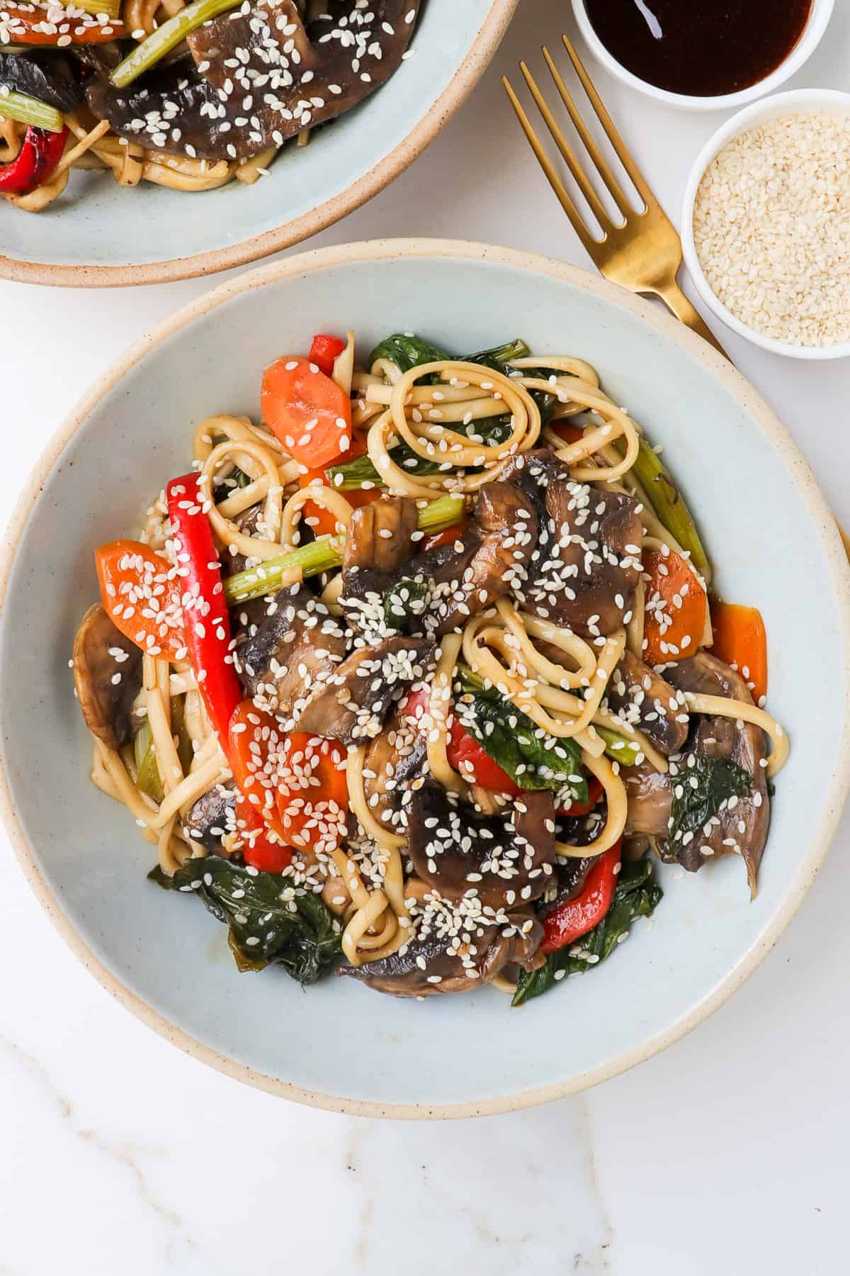 Teriyaki udon noodles with vegetables, mushrooms and sesame seeds sprinkled on top.
