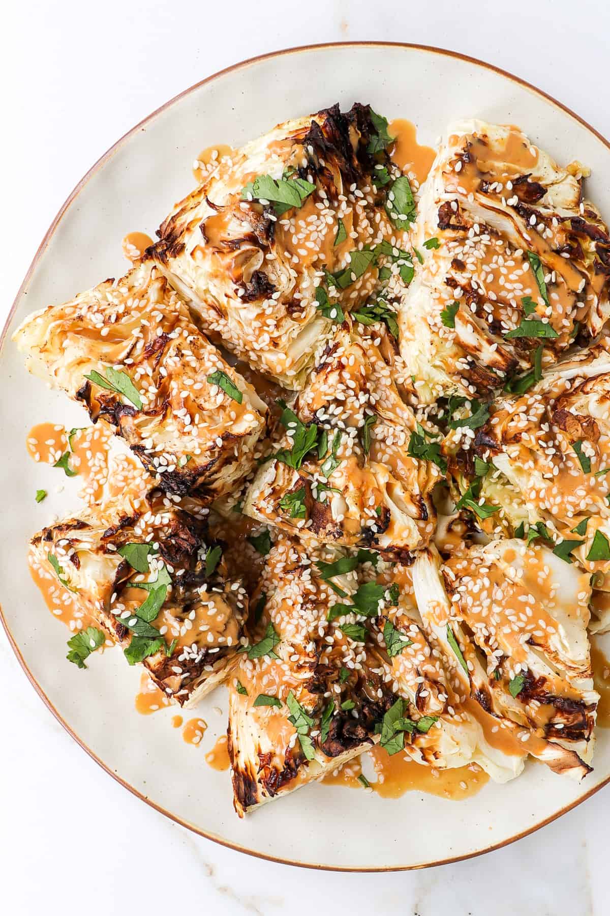 Roasted cabbage wedges on a plate. Peanut sauce is drizzled on top with sesame seeds and coriander leaves.