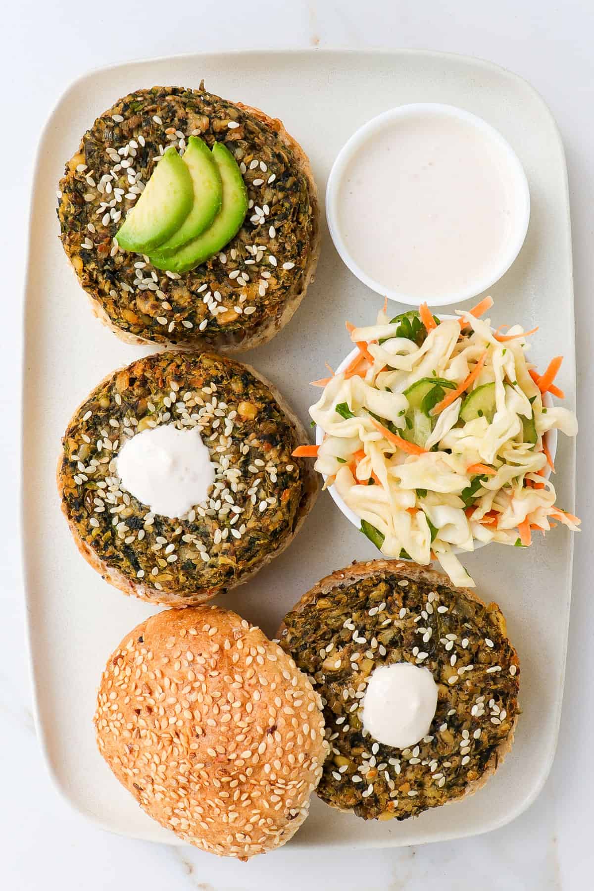 Mung bean veggie burgers on a platter with bread rolls, slaw, sauce and avocado.