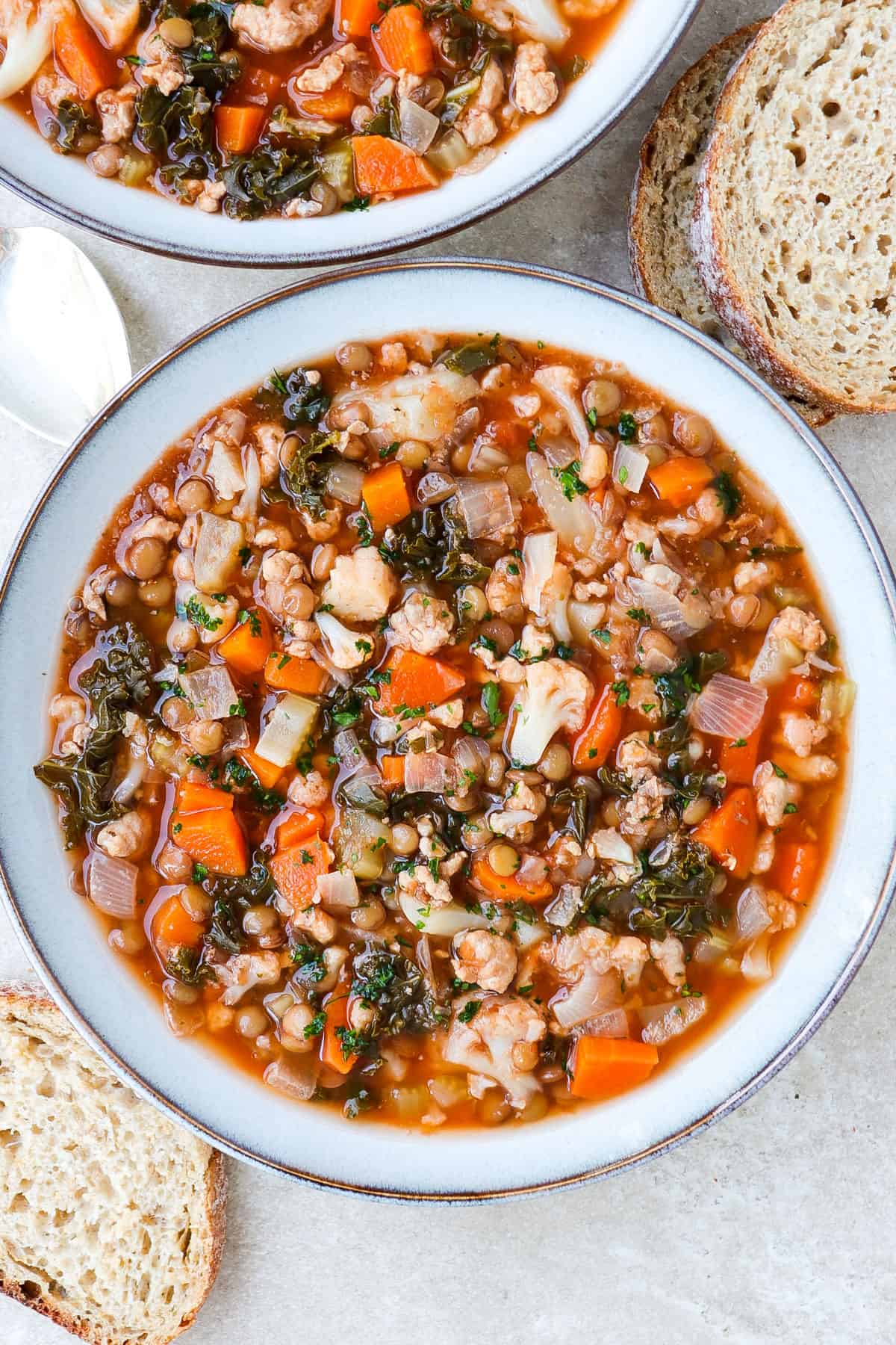 Soup in a bowl with sourdough and a silver spoon one the side.