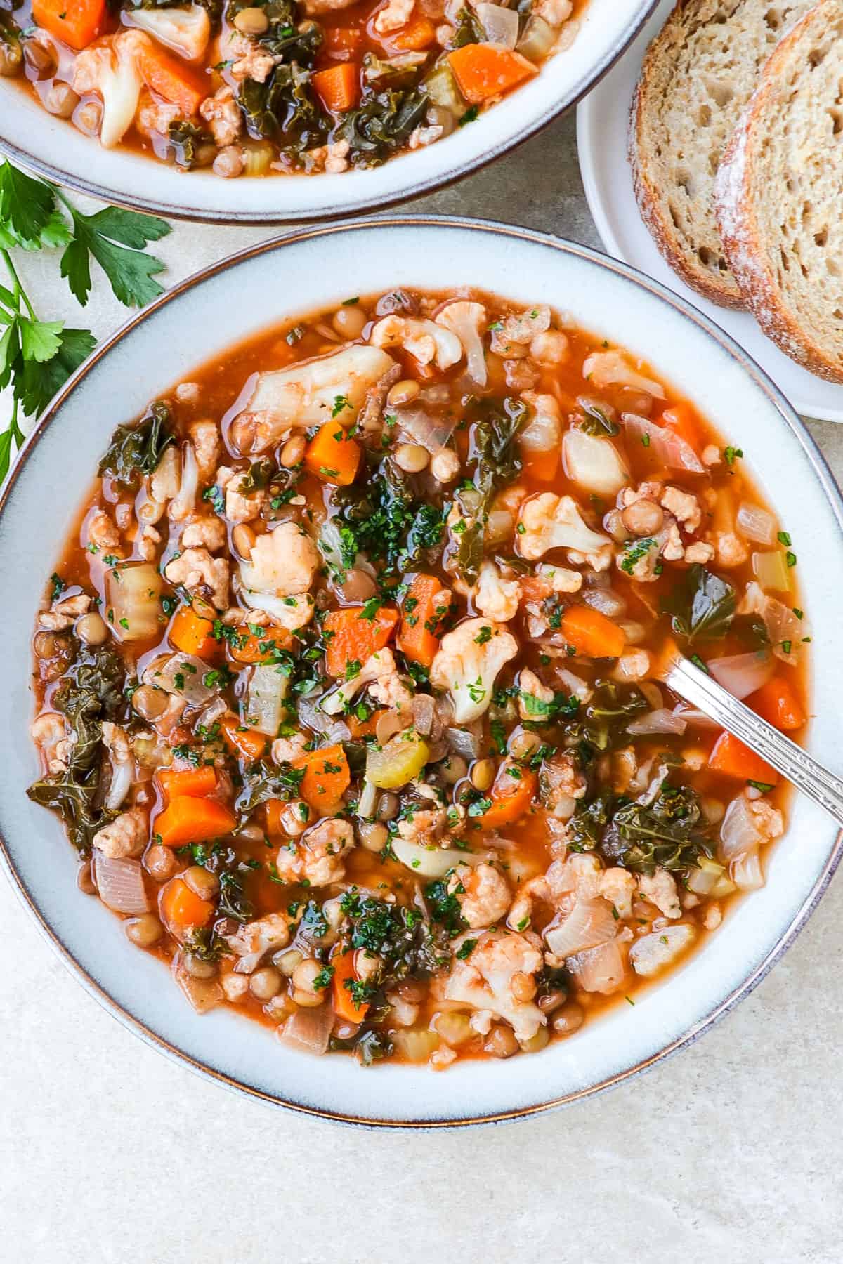 Soup in a bowl with a spoon. Bread and parsley on the side.