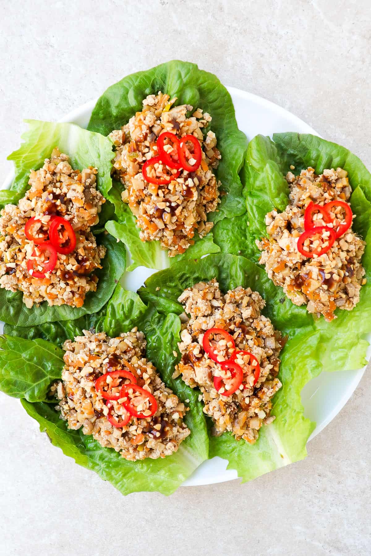 Five lettuce wraps on a plate topped with sliced chilli and crushed peanuts.