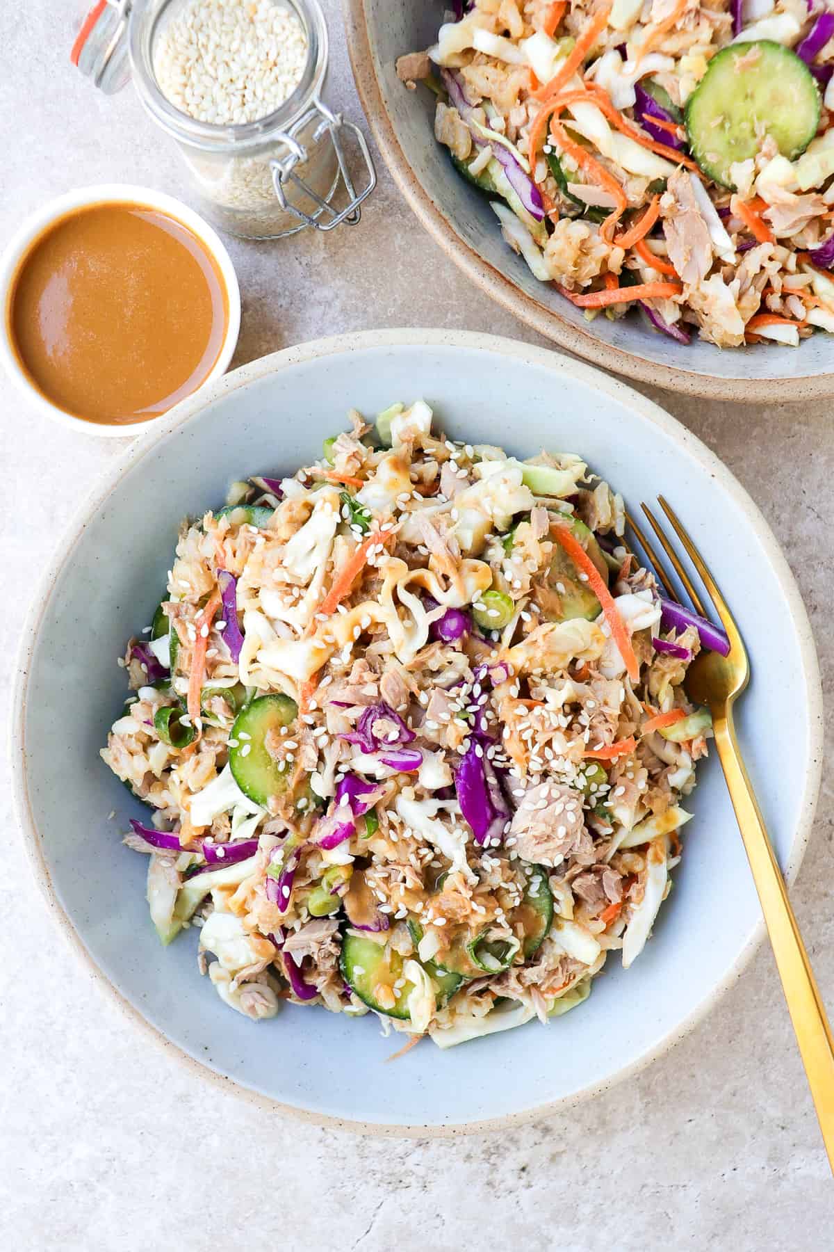 Cabbage tuna salad in two bowls with gold fork and peanut sauce in a side dish.