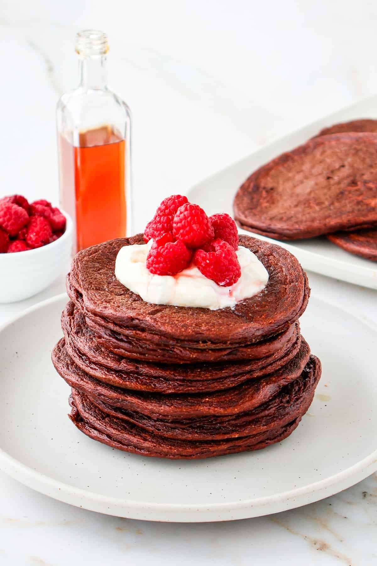 Side shot of chocolate protein pancakes with yoghurt and raspberries on top.
