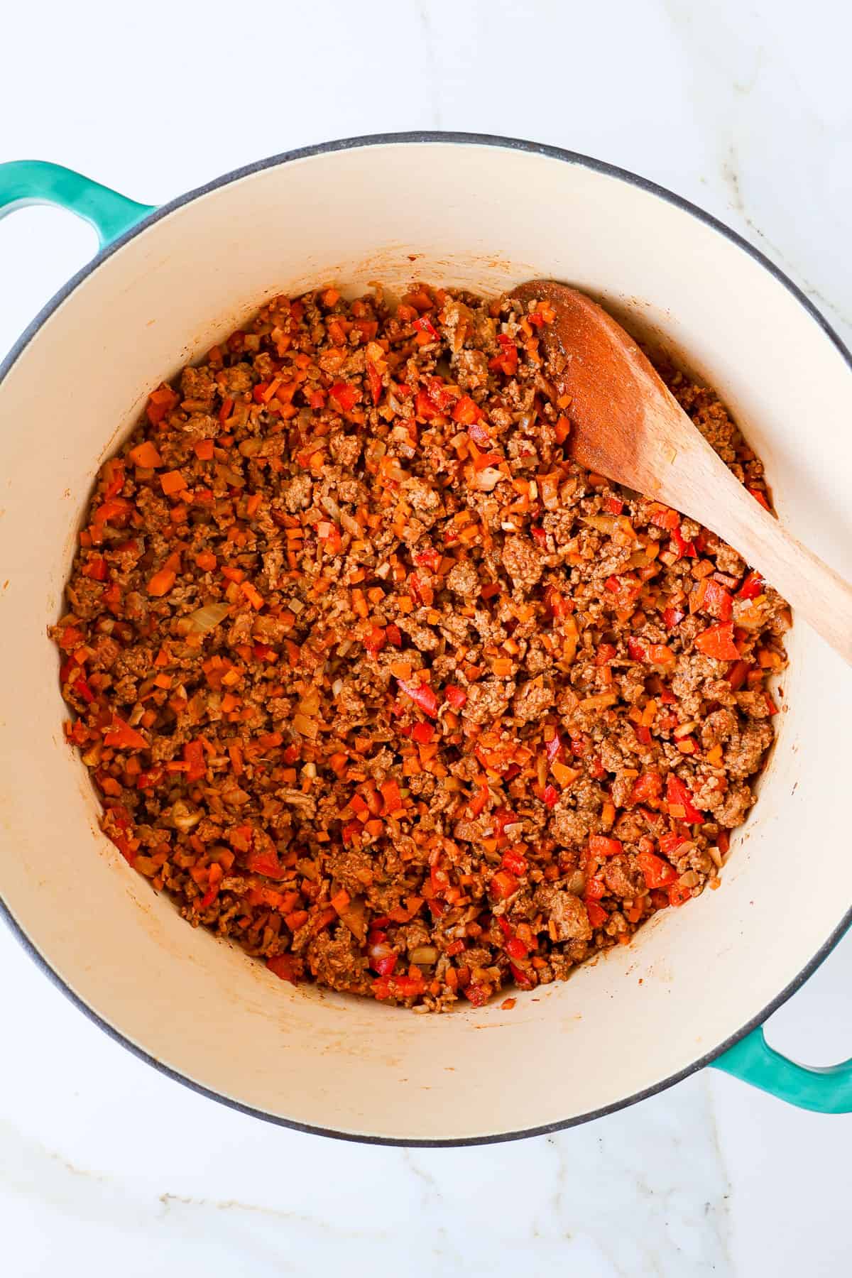 Ground meat and veggies in a pot with a wooden spoon.