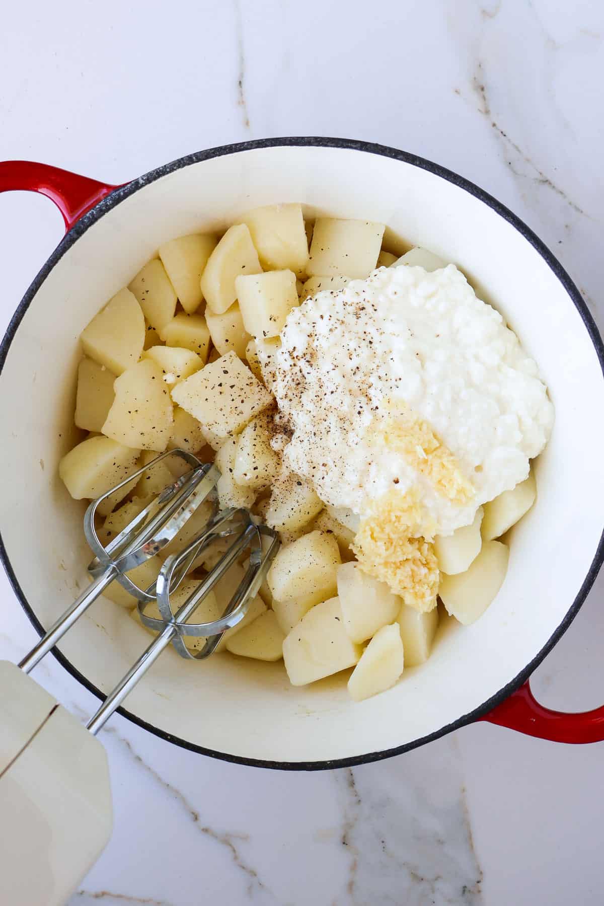 Cooked potatoes in a pot with cottage cheese, butter, milk, garlic, salt, pepper and a blender.