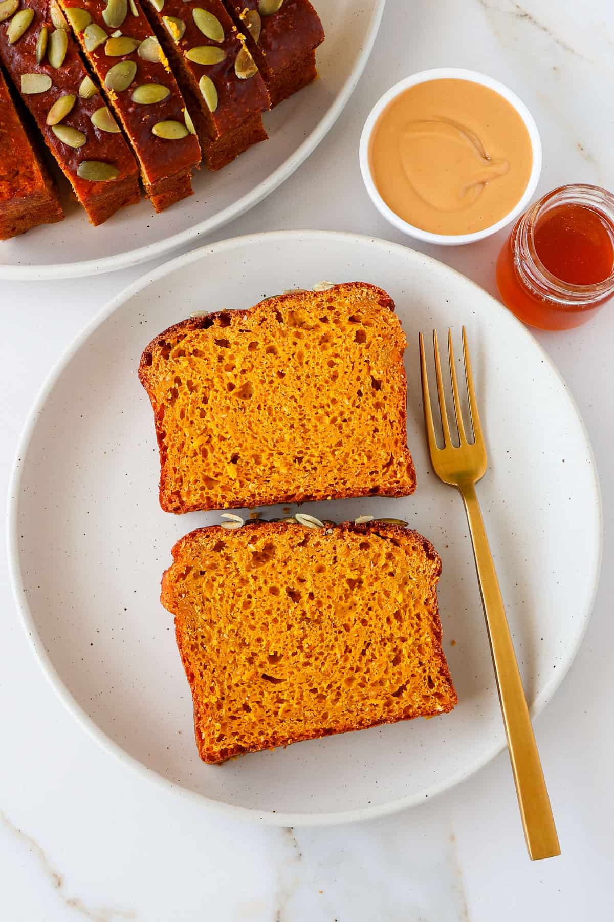 Two slices of pumpkin bread non a plate with a gold fork.