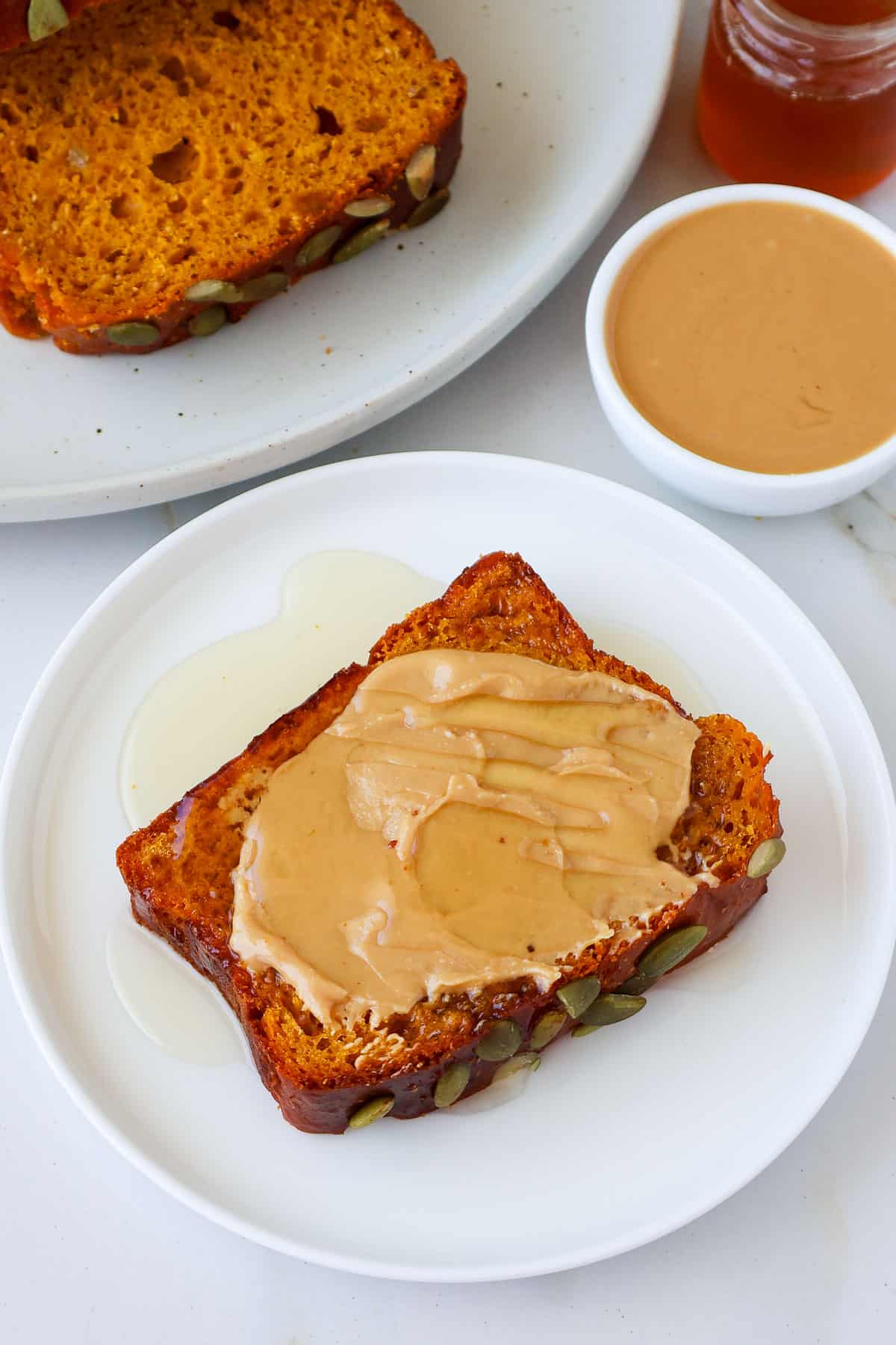 Sliced of pumpkin protein bread of a plate topped with nut butter and maple syrup.