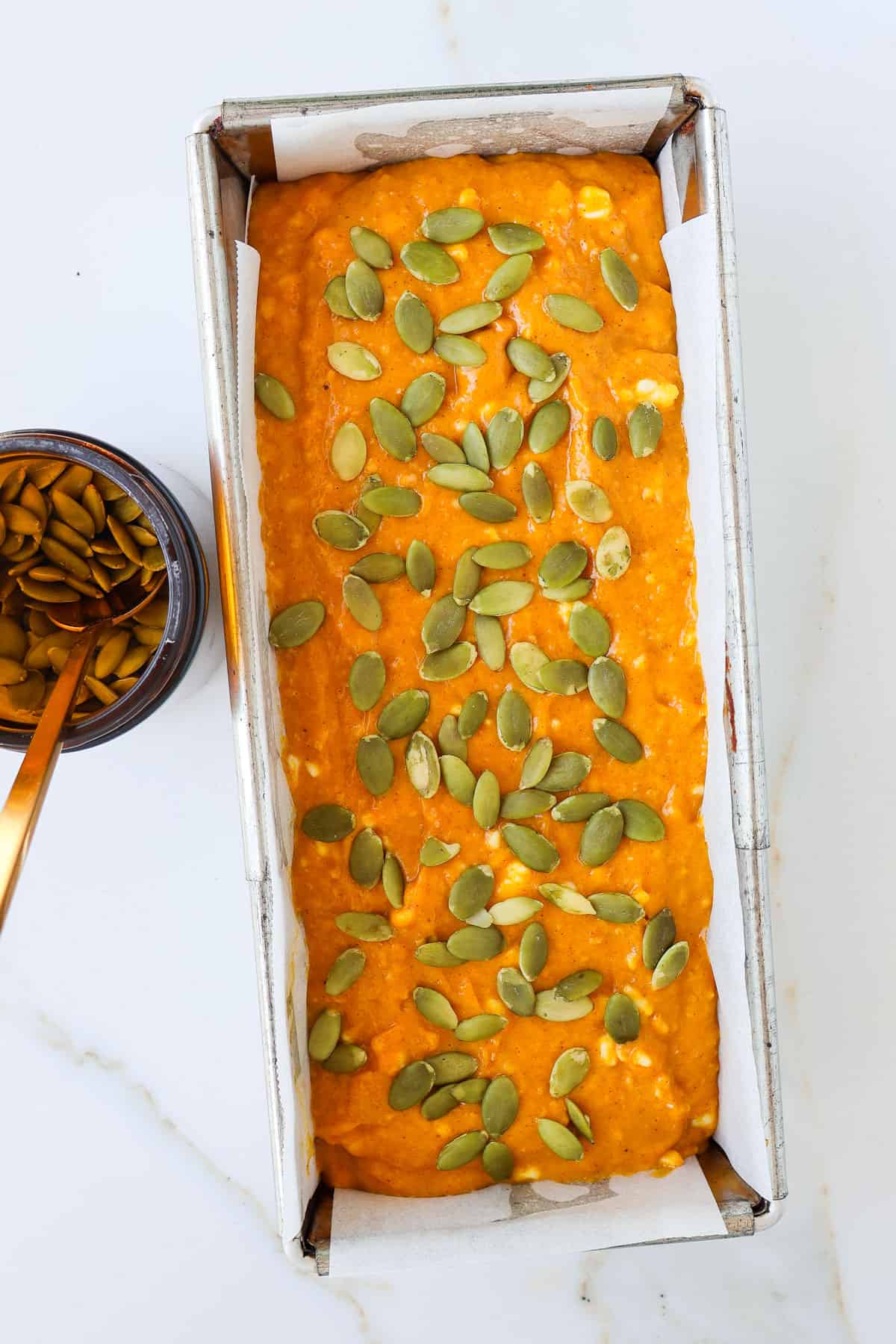 Batter poured into a loaf pan topped with pumpkin bread.