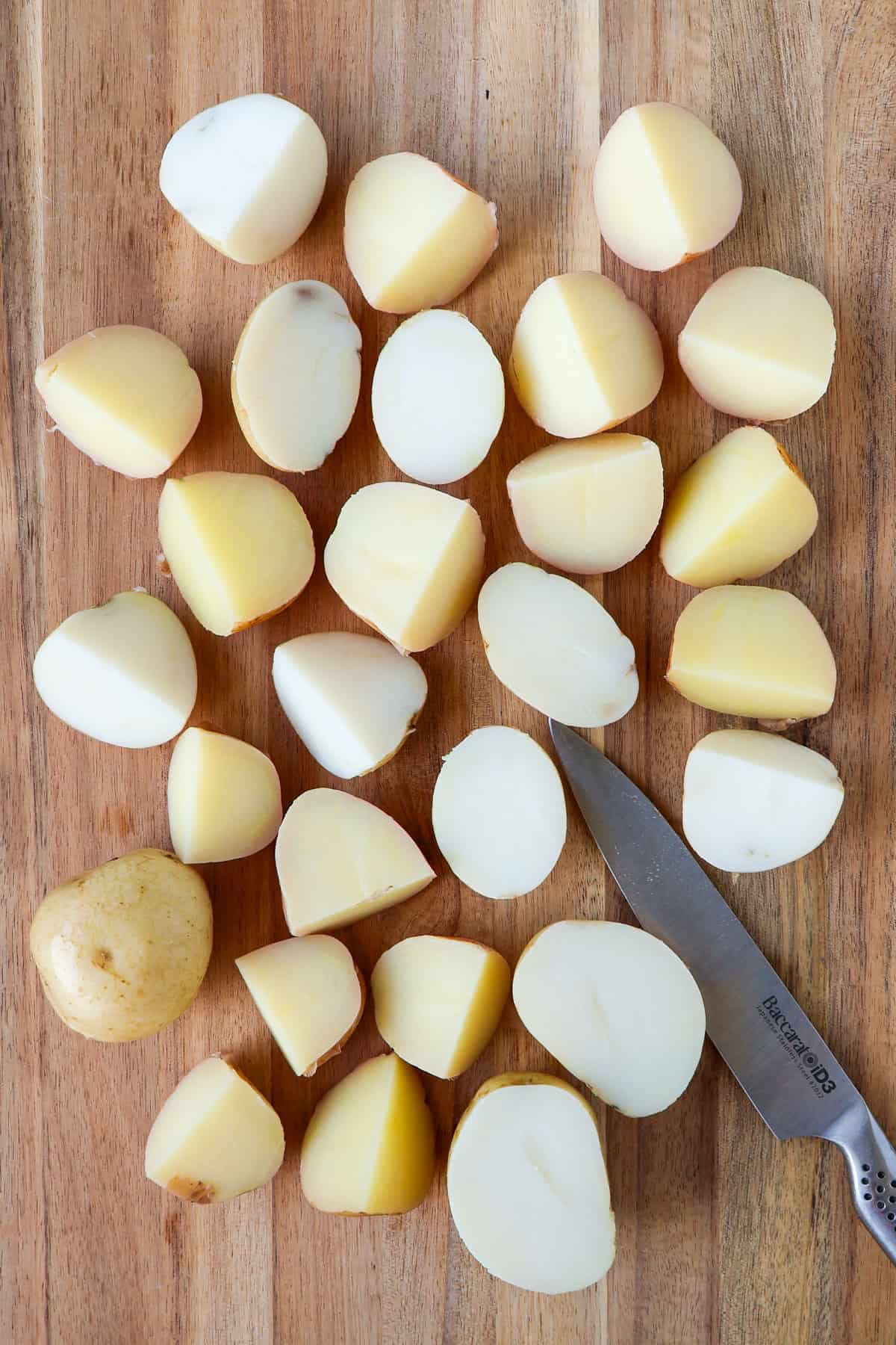 Boiled potatoes on a wooden board being cut in half.
