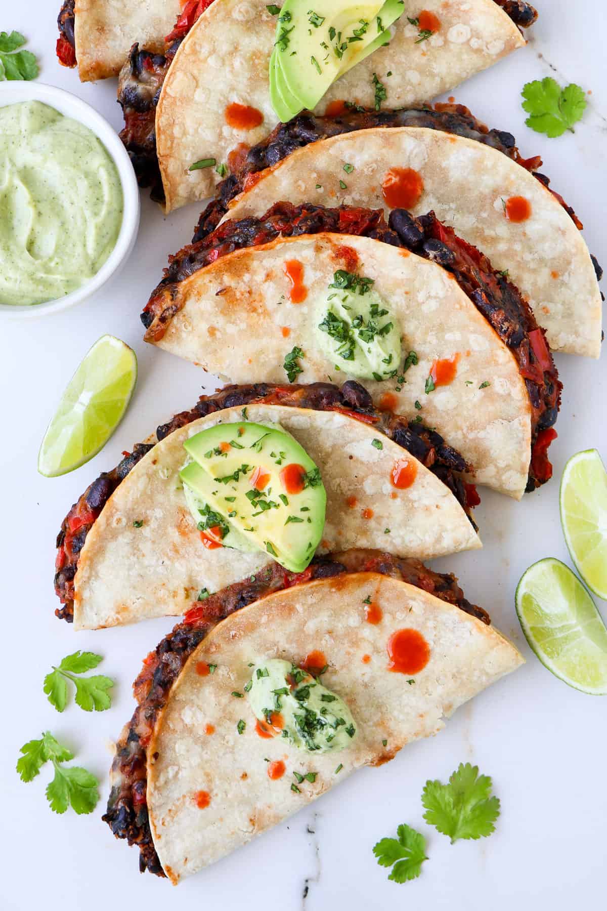 Close up shot of black bean tacos topped with avocado, who sauce and crema.