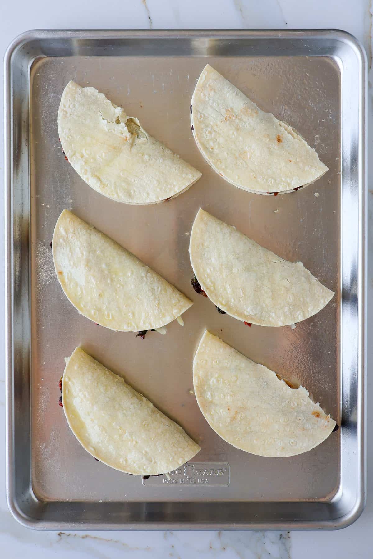 Folded tacos on sheet pan before being backed.