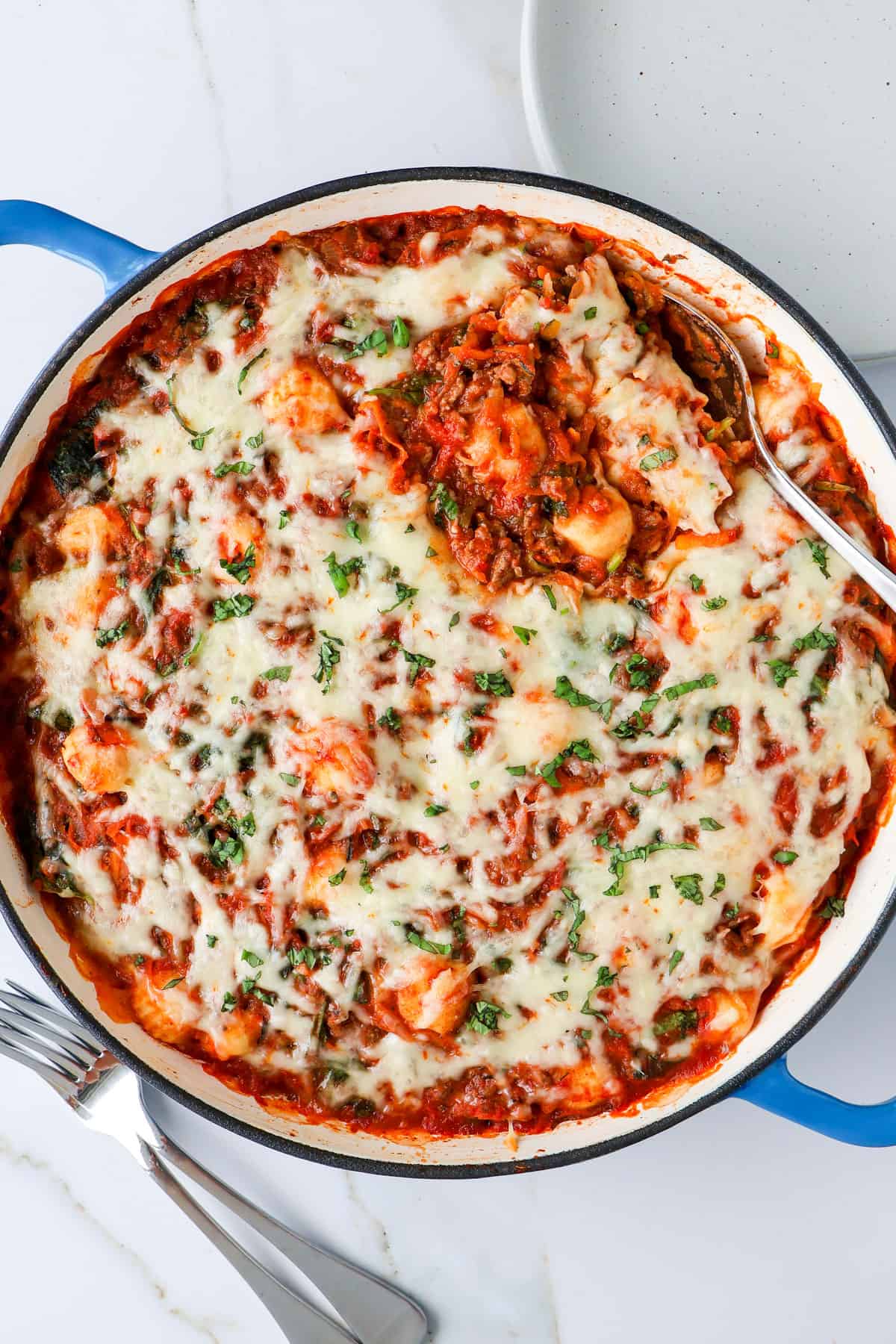 Baked gnocchi bolognese in a baking dish with a spoon.