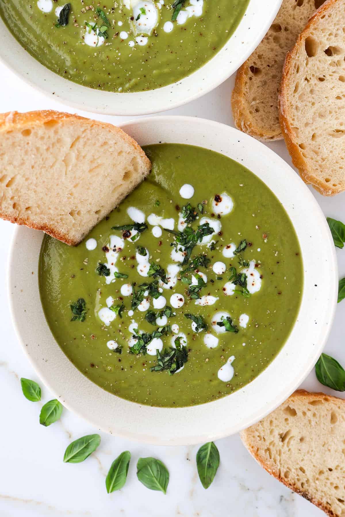 Green soup in a bowl with cream on top and bread dipped in.