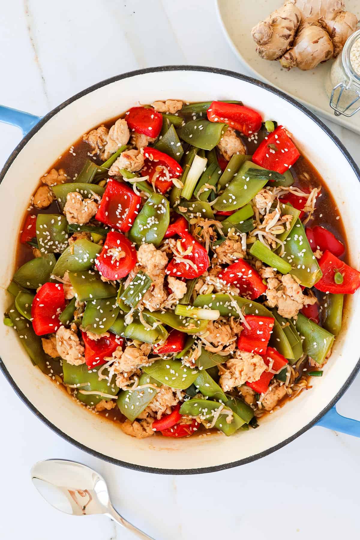 Ground chicken stir fry with veggies in a skillet with spoon on the bottom.