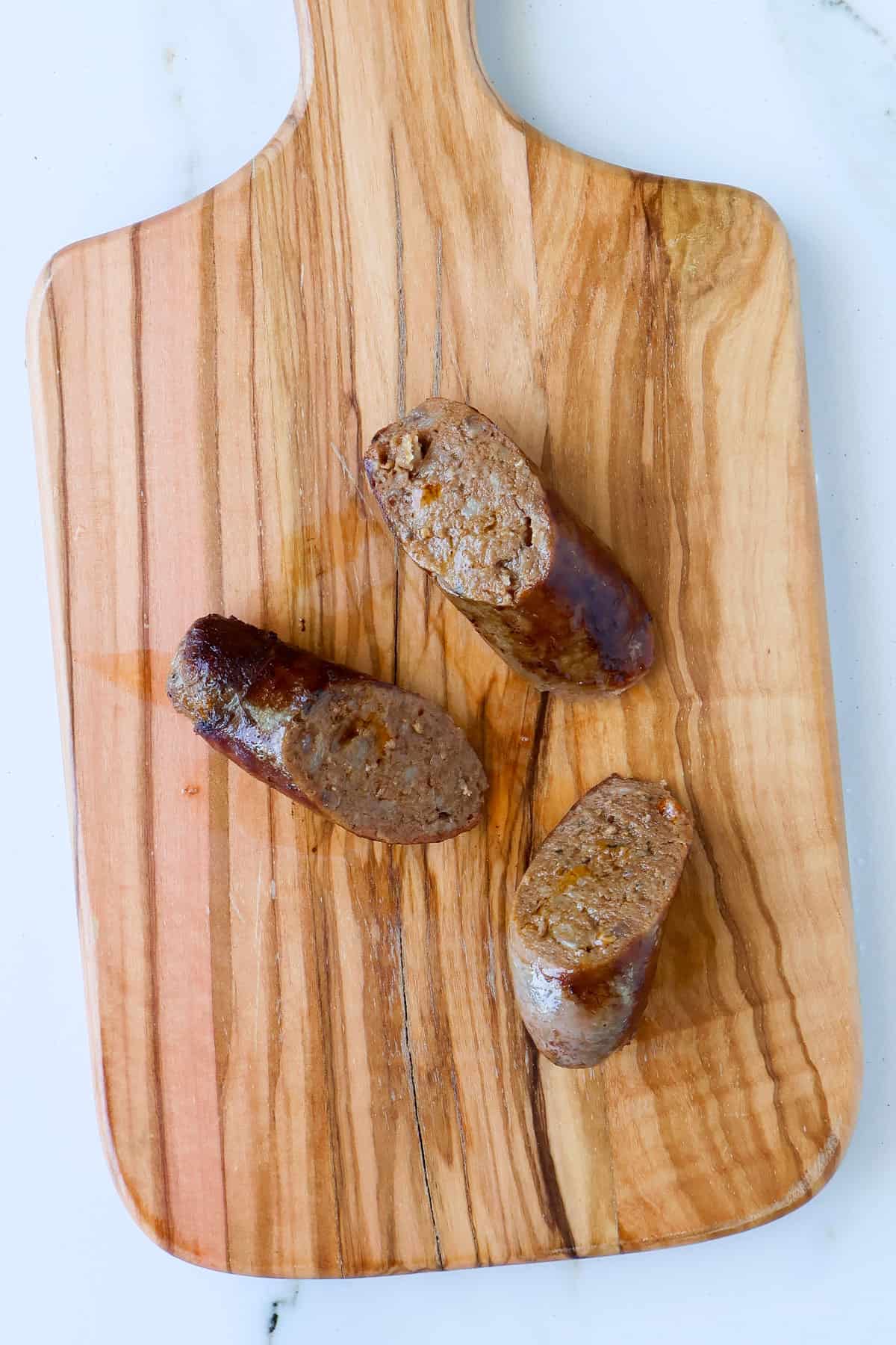 Cooked sausages sliced on wooden board.